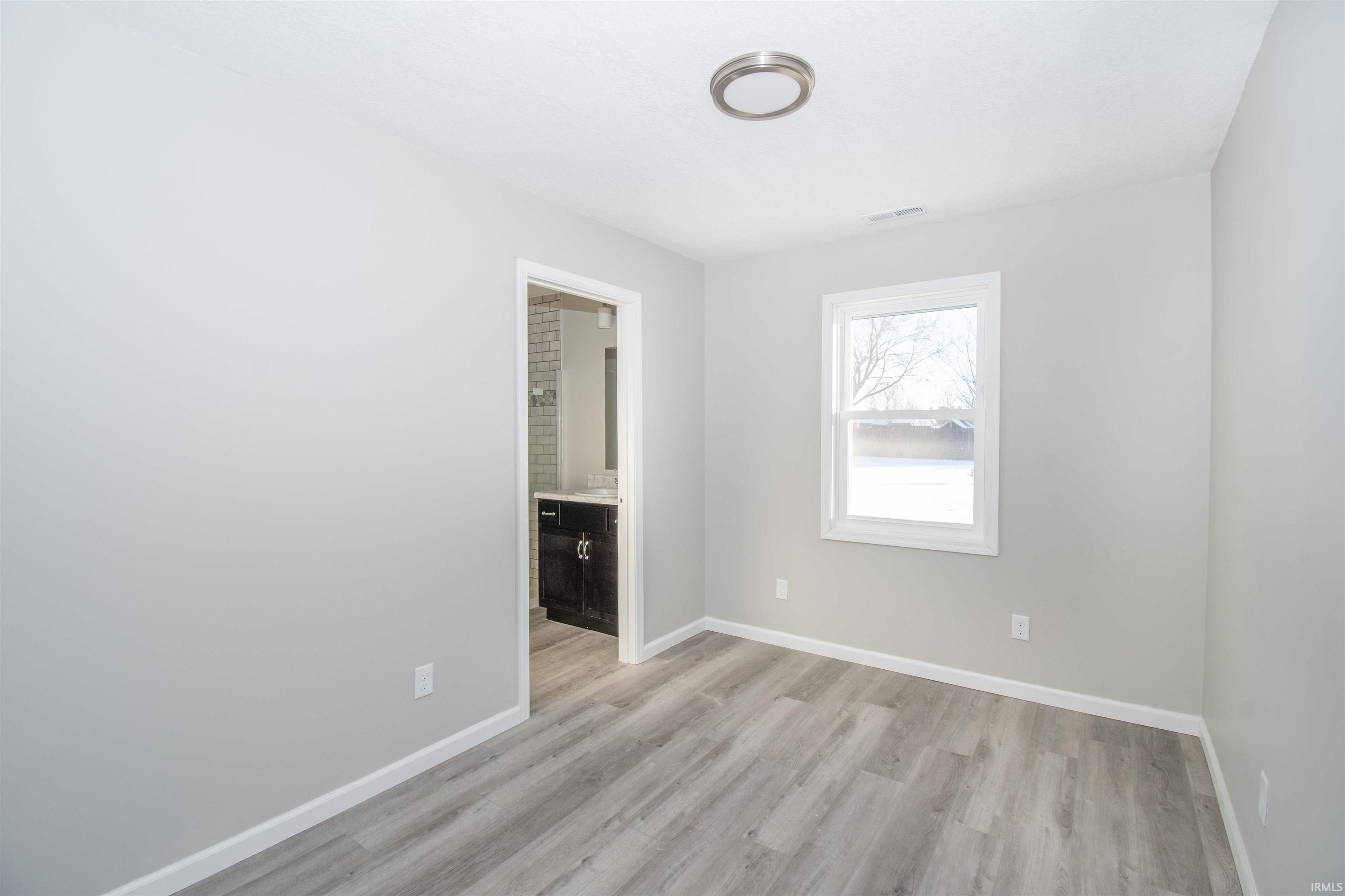 Unfurnished bedroom with light wood-style floors and connected bathroom