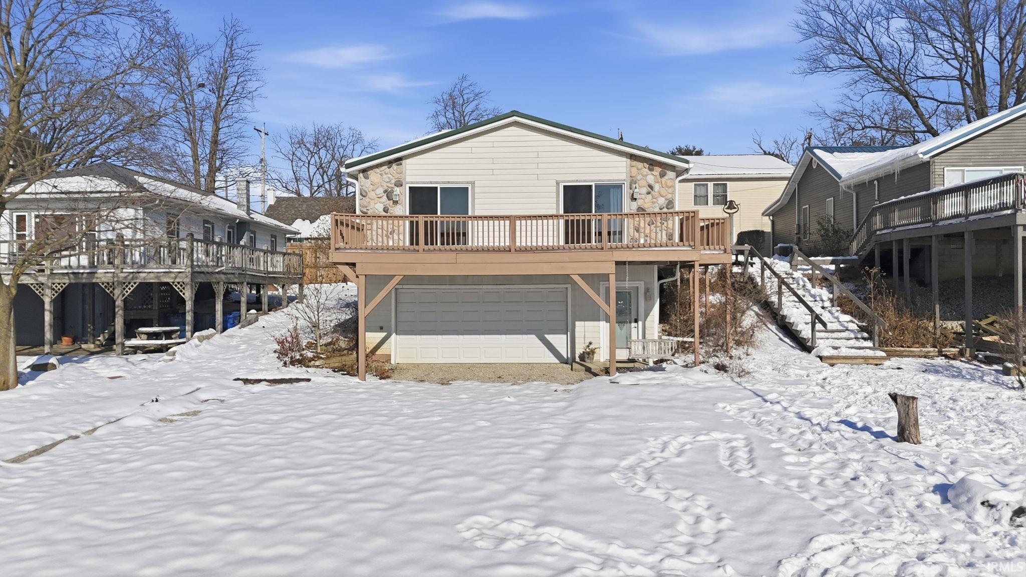 Snow covered back of property with a deck and a garage