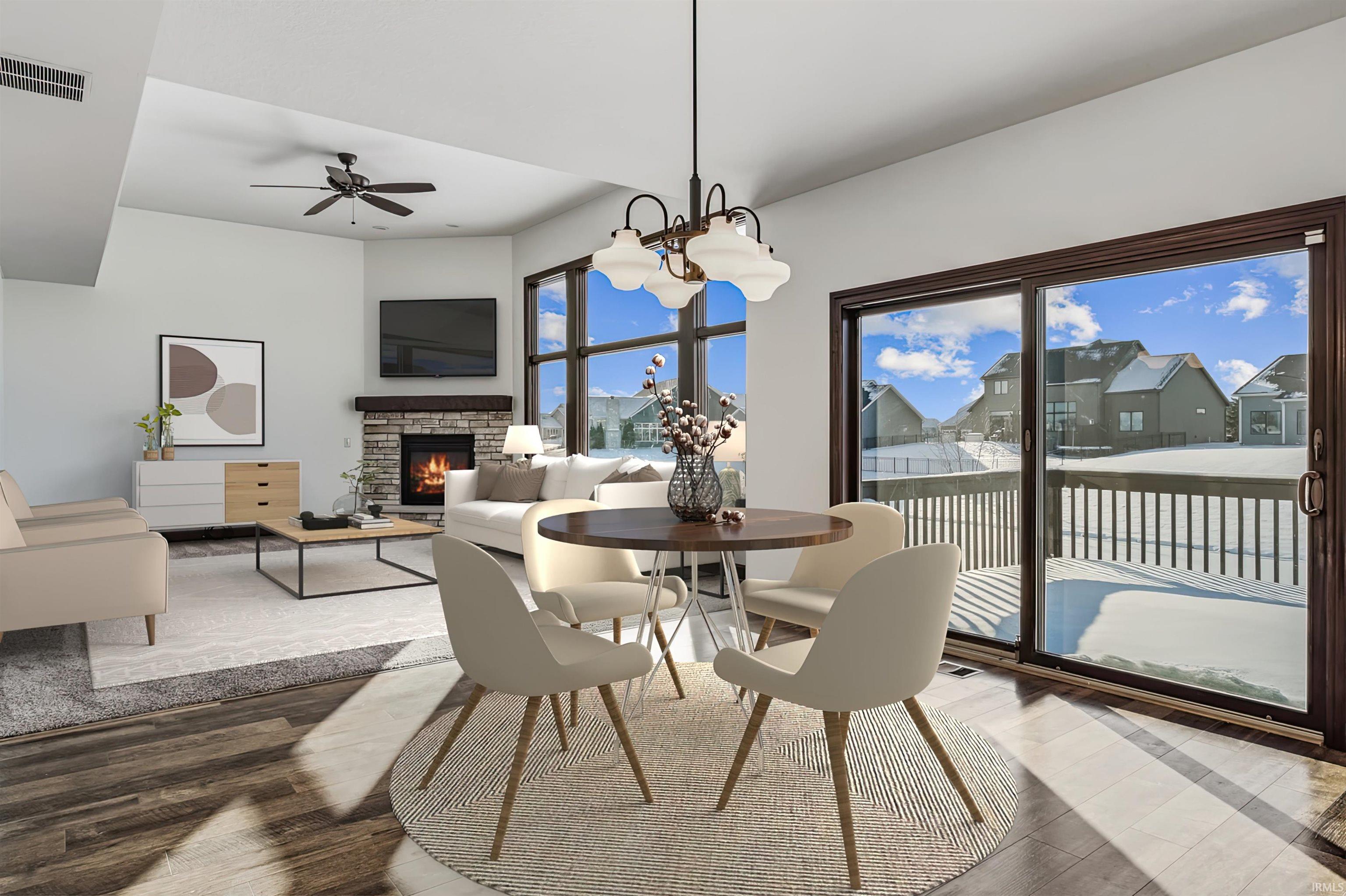 Dining room with wood finished floors, a stone fireplace, a chandelier, and a ceiling fan