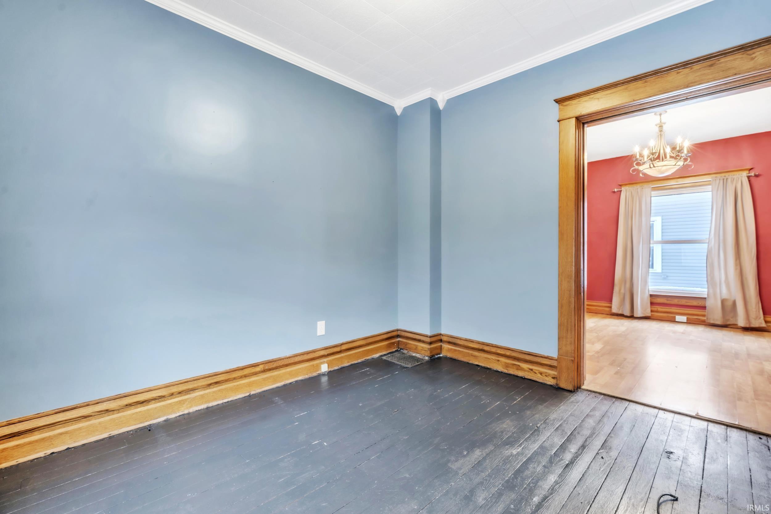 Spare room with dark wood-type flooring, a chandelier, and ornamental molding