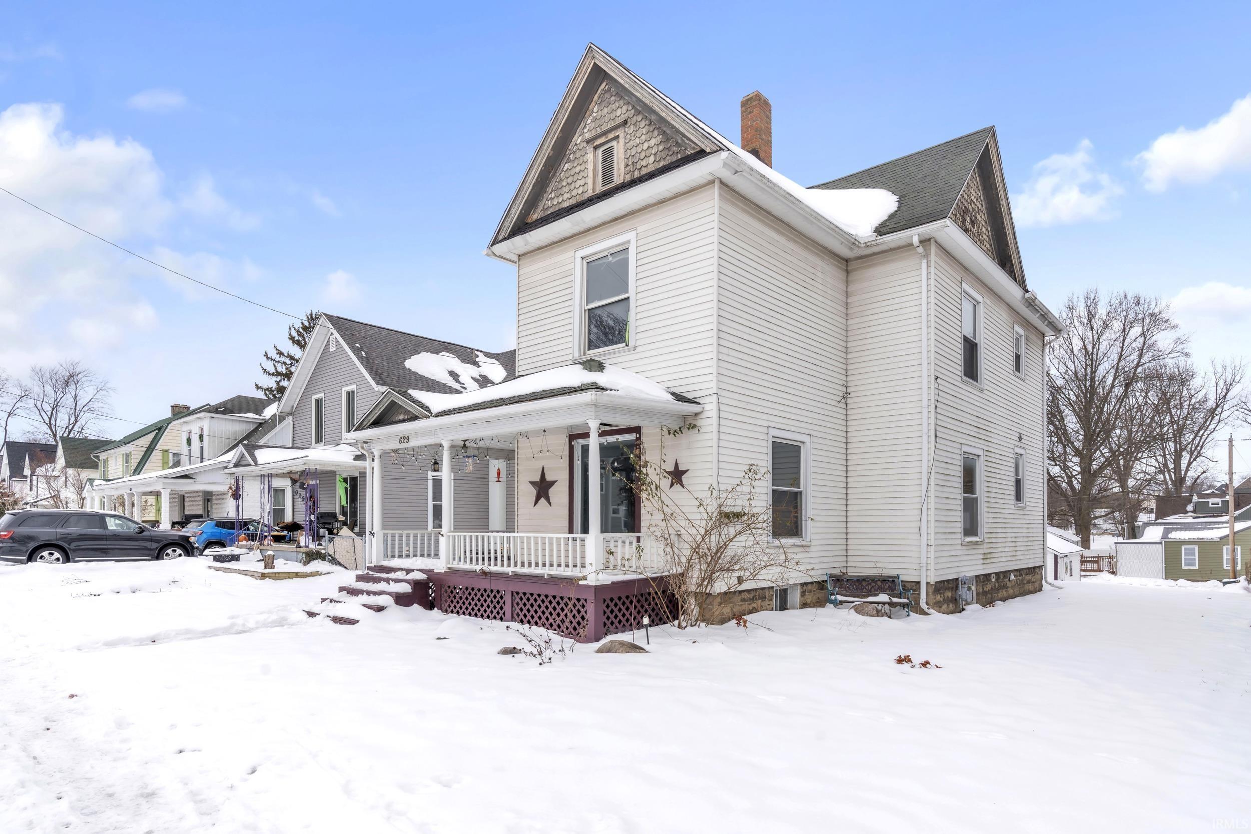 View of snow covered exterior featuring covered porch and a chimney