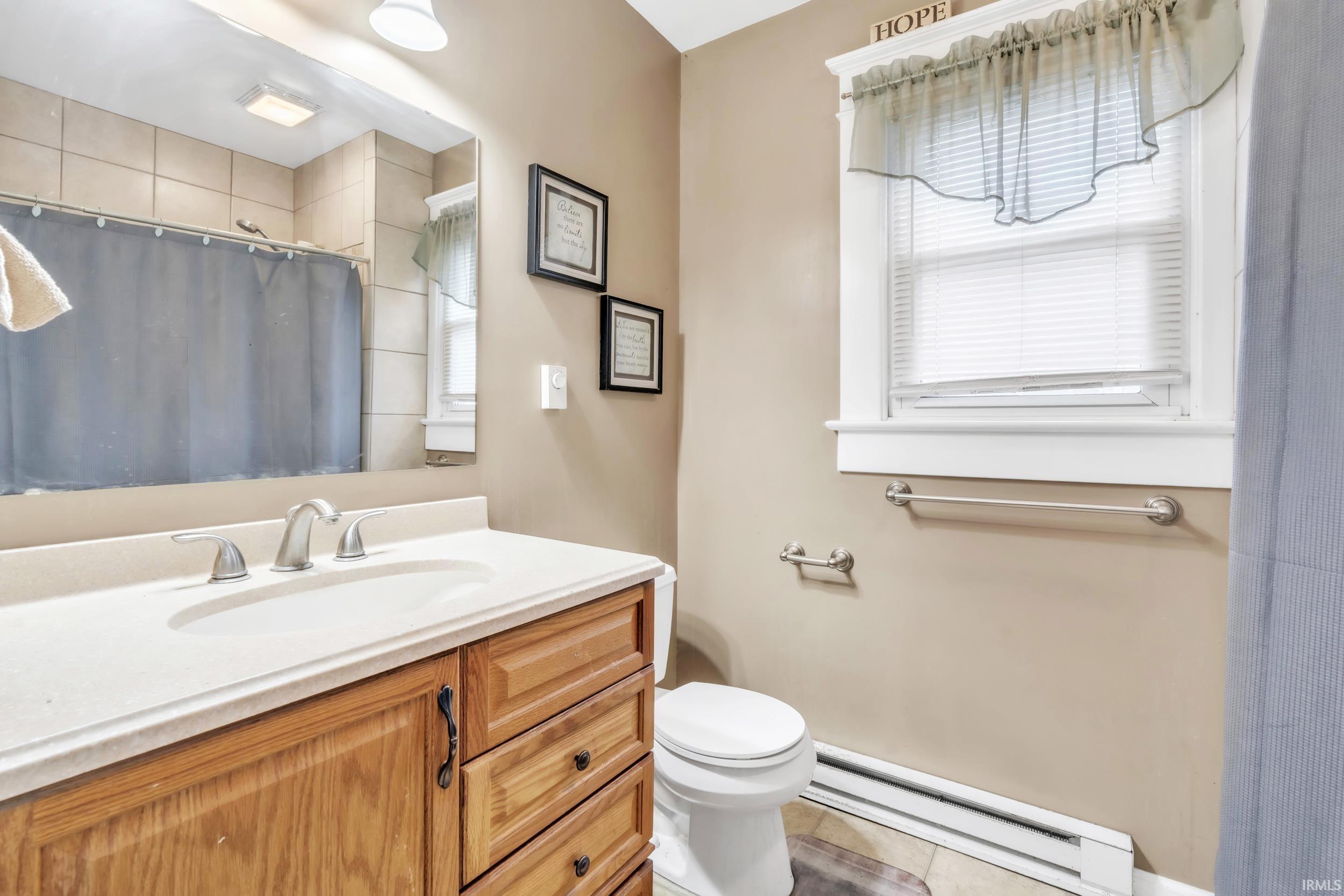 Full bathroom with baseboard heating, vanity, a shower with curtain, and tile patterned flooring
