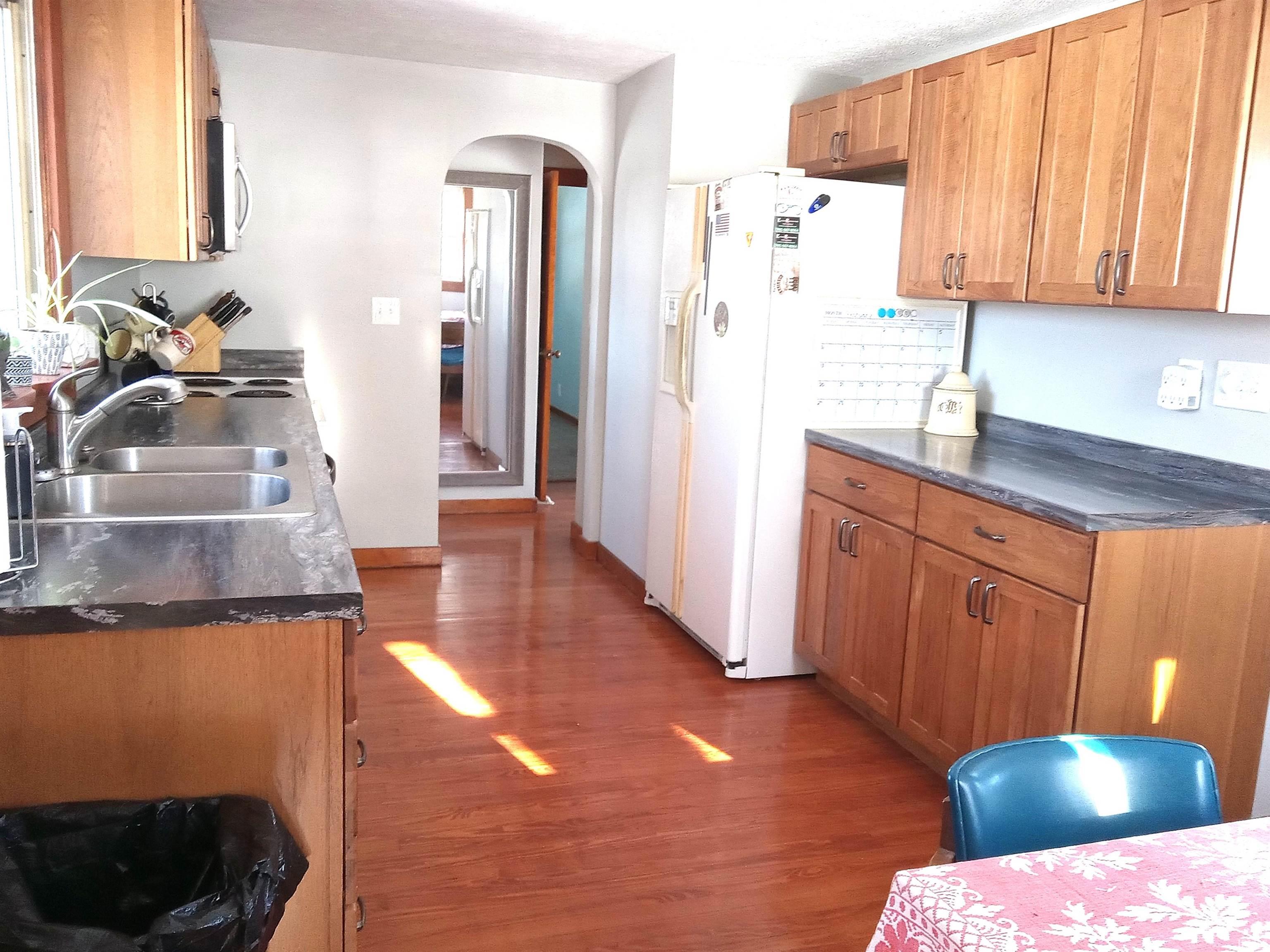 Kitchen featuring dark countertops, brown cabinetry, arched walkways, white fridge with ice dispenser, and dark wood-style flooring