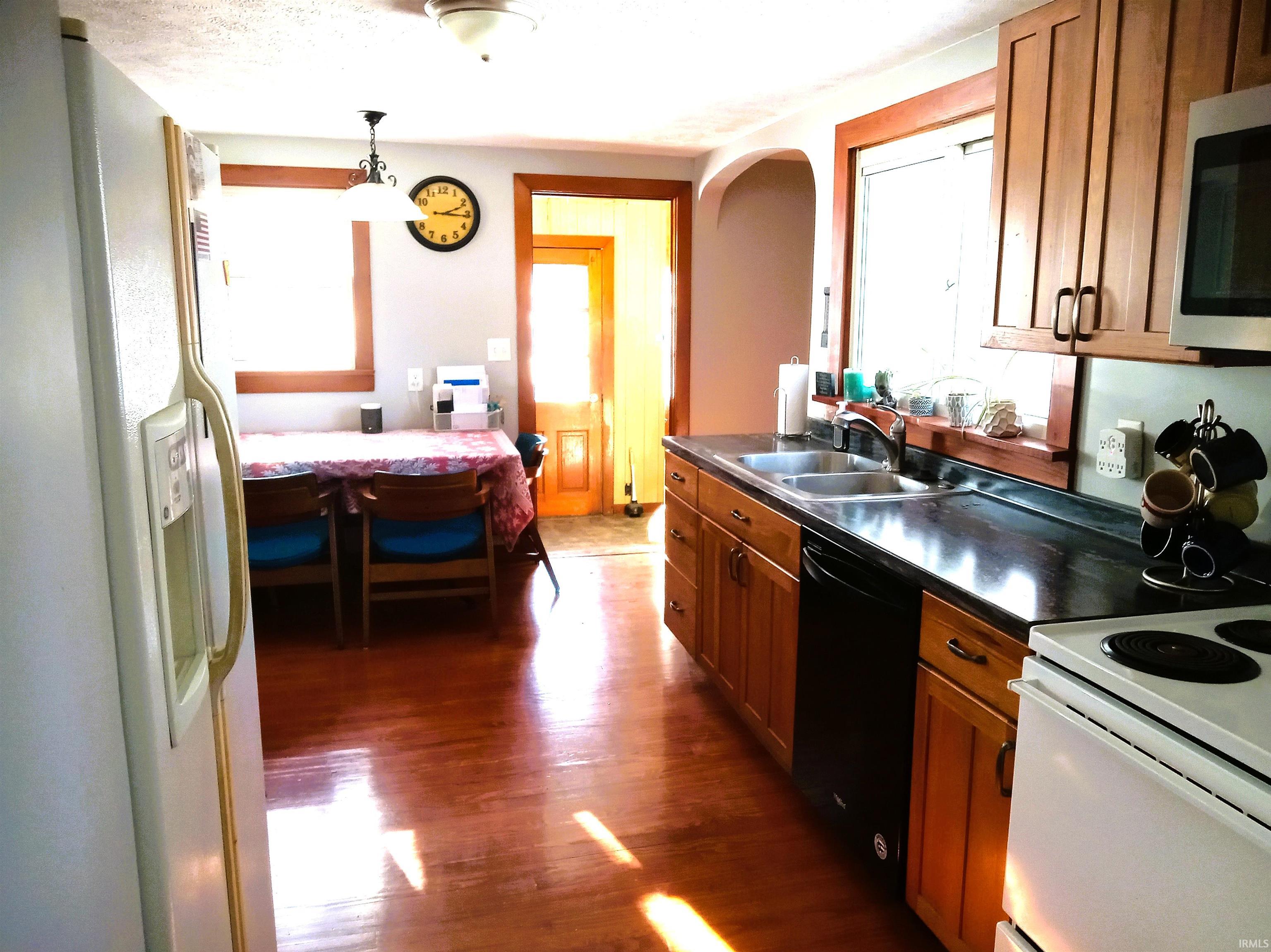 Kitchen featuring dark countertops, brown cabinetry, white appliances, dark wood-type flooring, and a textured ceiling