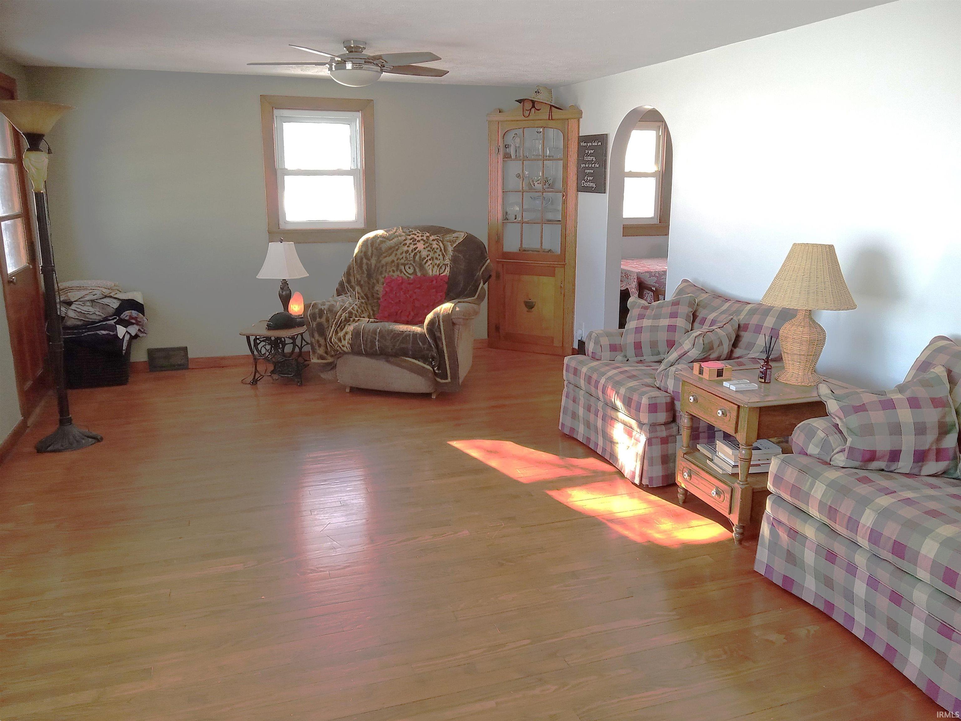Living room with light wood-type flooring, a ceiling fan, and arched walkways