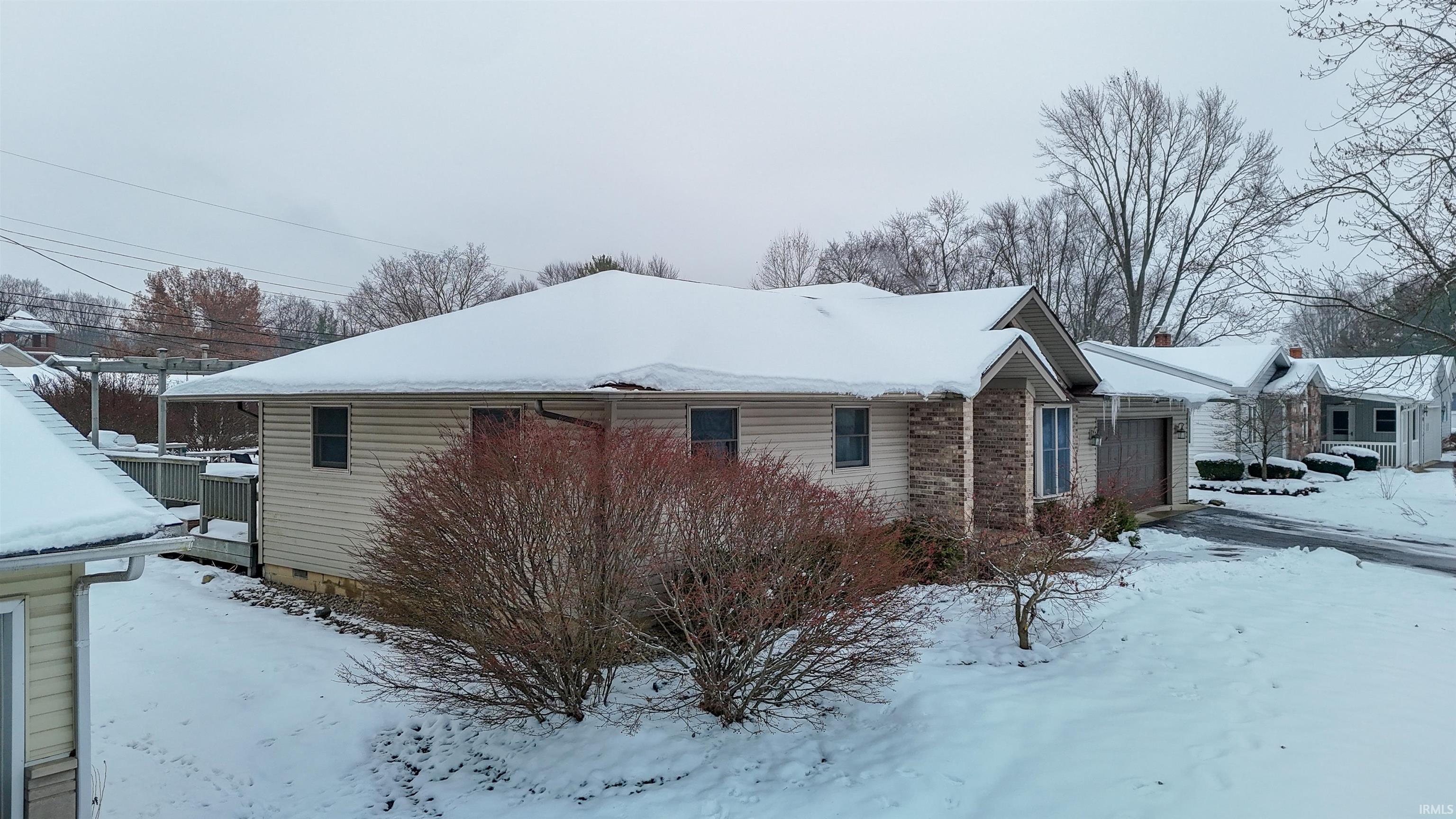View of snowy exterior with a garage and brick siding
