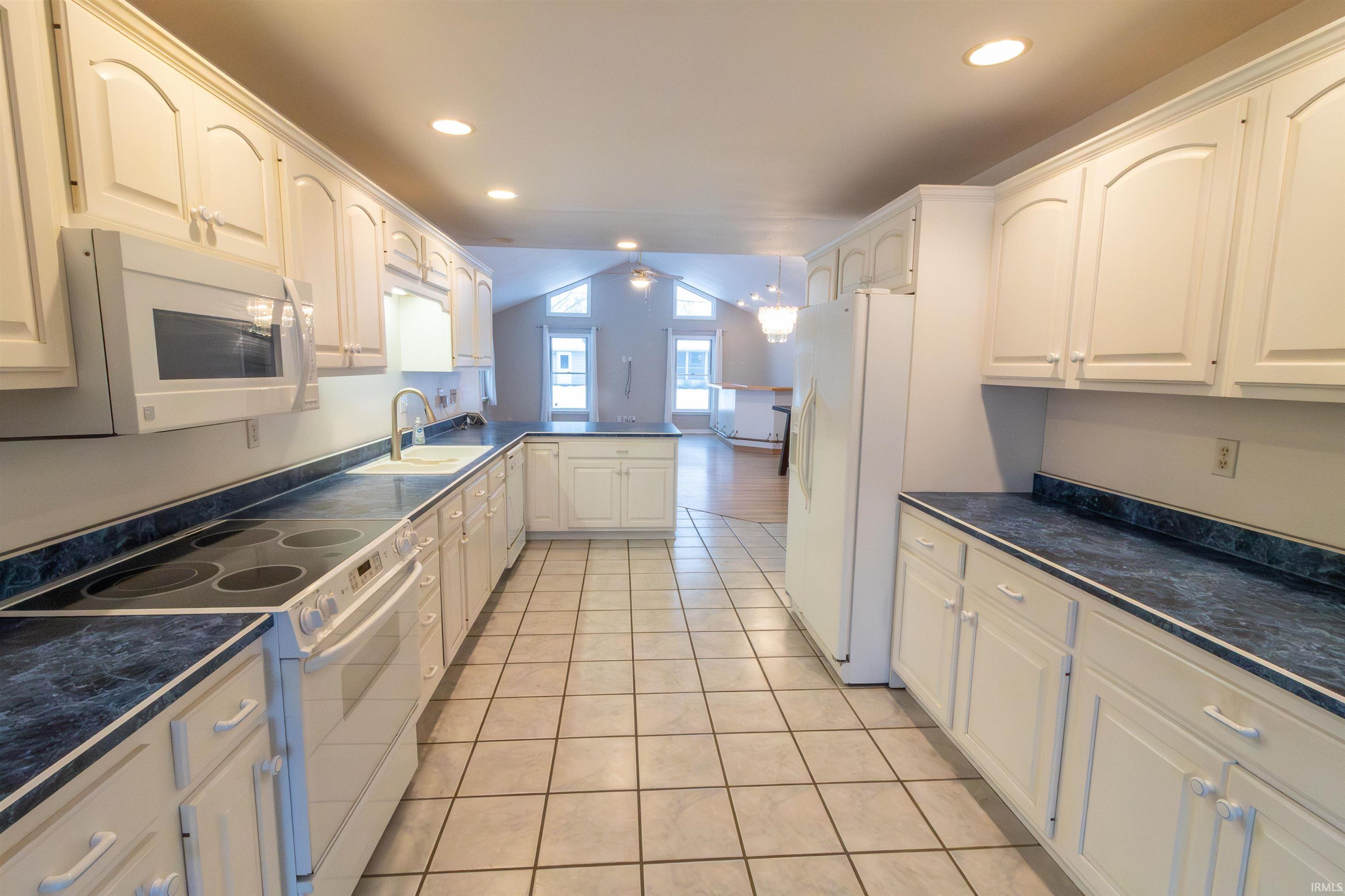 Kitchen with dark countertops, white appliances, vaulted ceiling, a peninsula, and white cabinets
