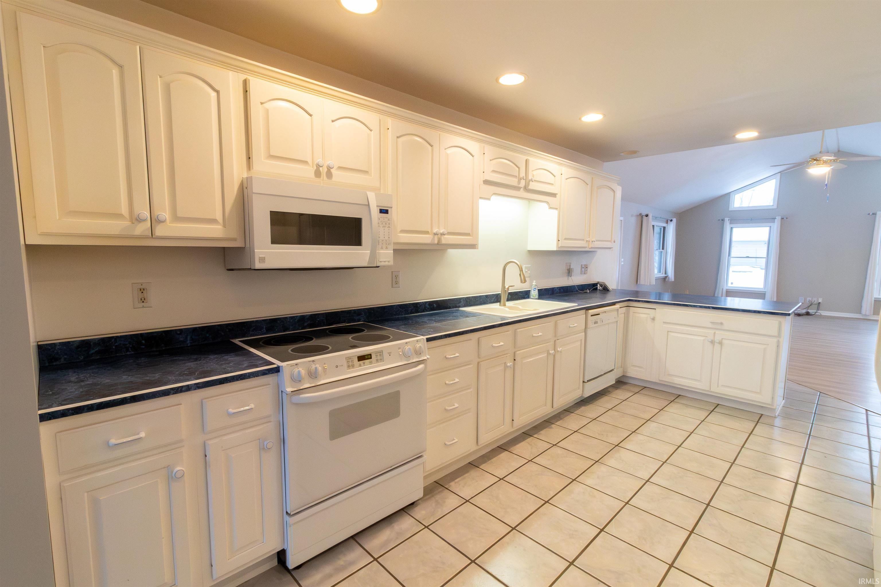 Kitchen featuring dark countertops, vaulted ceiling, white appliances, ceiling fan, and recessed lighting