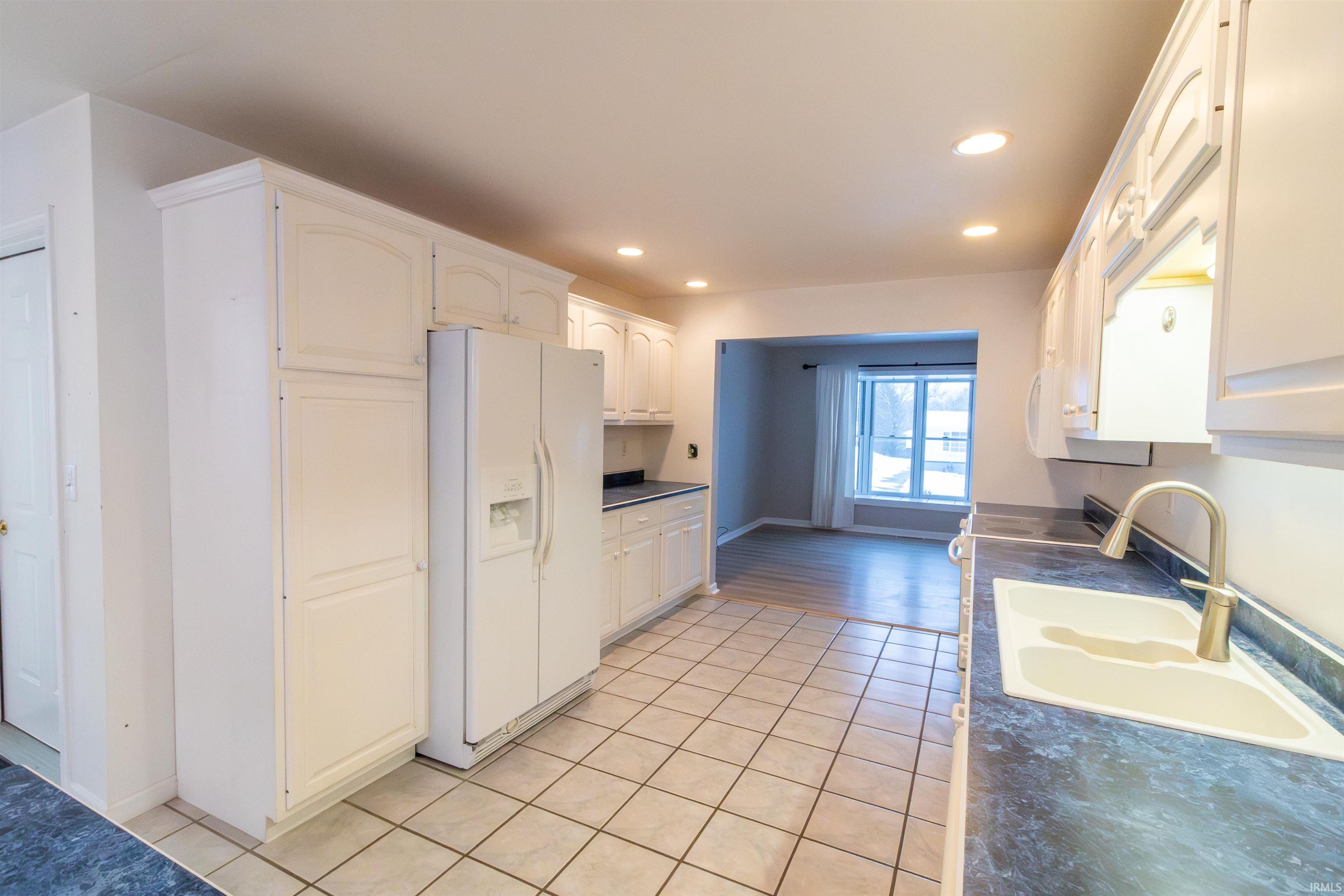 Kitchen with dark countertops, white appliances, white cabinets, recessed lighting, and light tile patterned floors