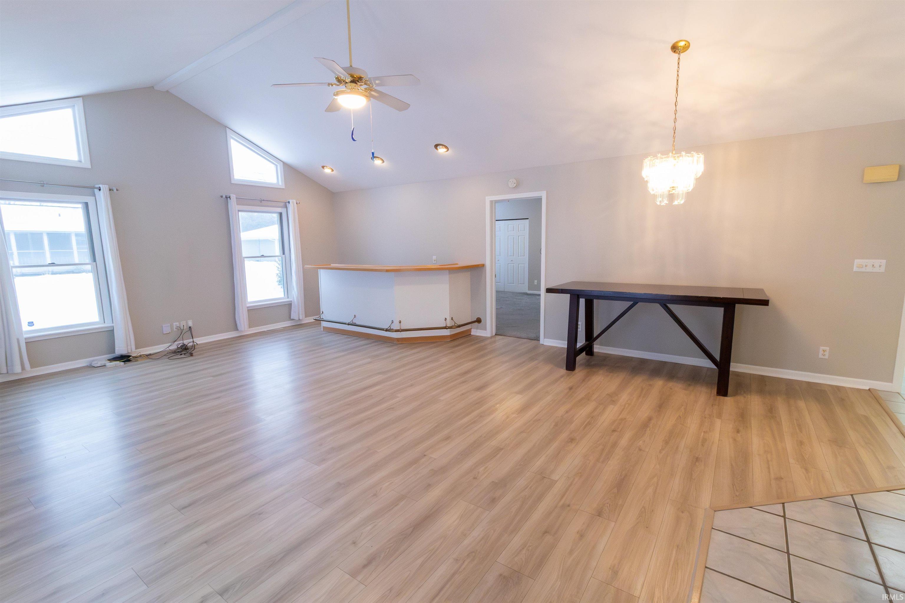 Unfurnished living room with light wood finished floors, a ceiling fan, a chandelier, high vaulted ceiling, and a baseboard radiator