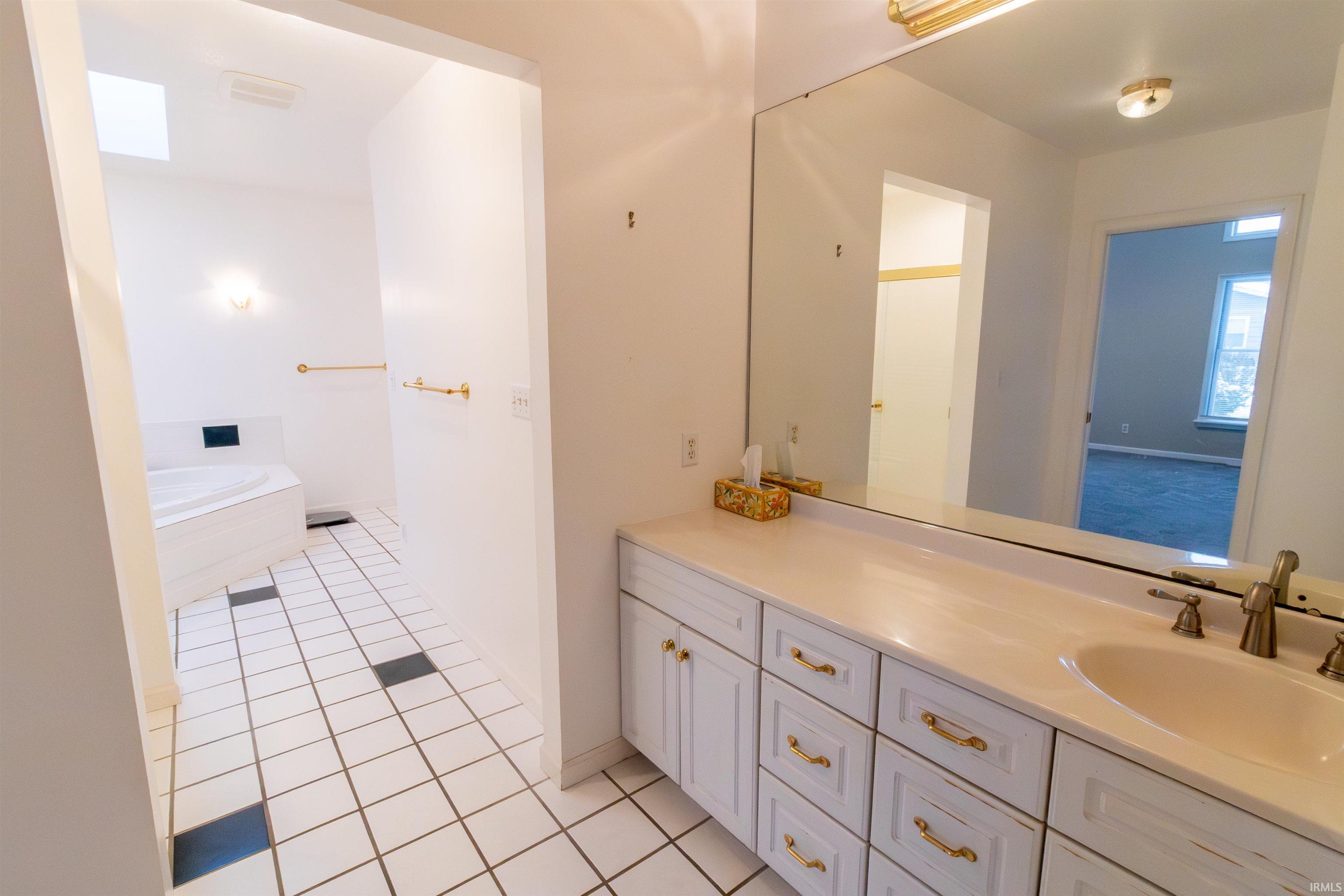 Full bathroom featuring a garden tub, vanity, a skylight, and light tile patterned flooring