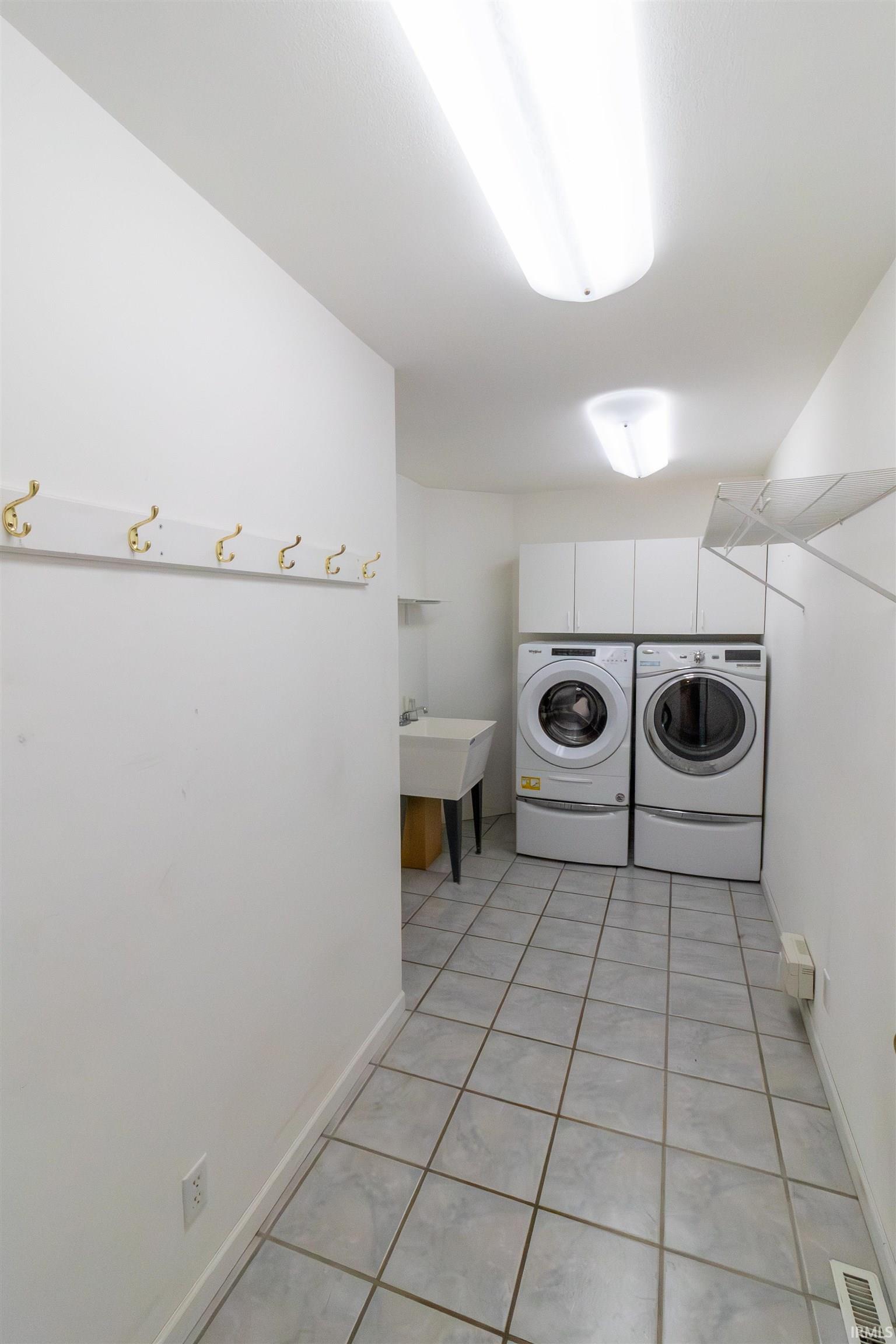 Laundry room with independent washer and dryer and light tile patterned flooring