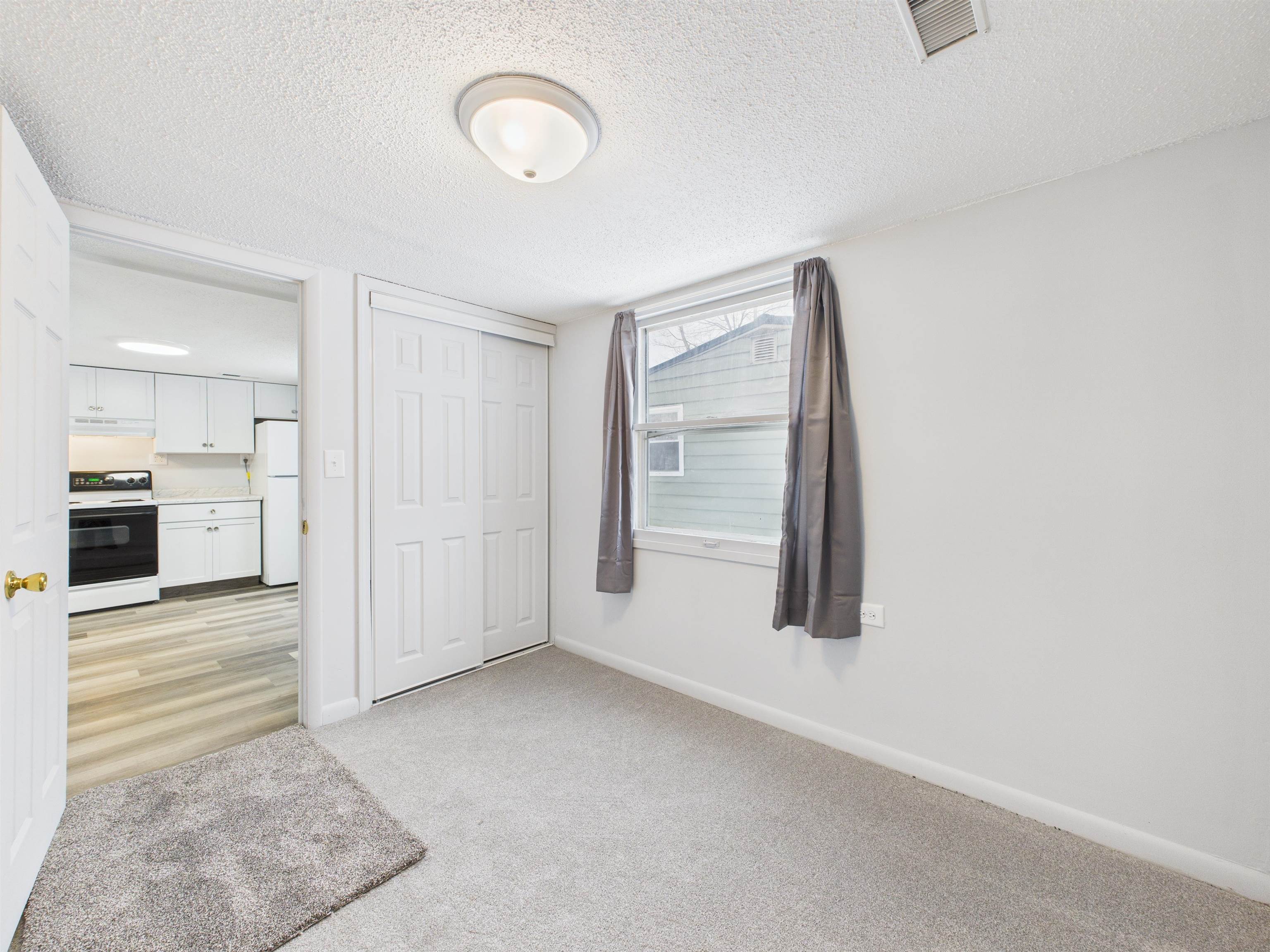 Unfurnished bedroom with a textured ceiling, light carpet, a closet, and freestanding refrigerator