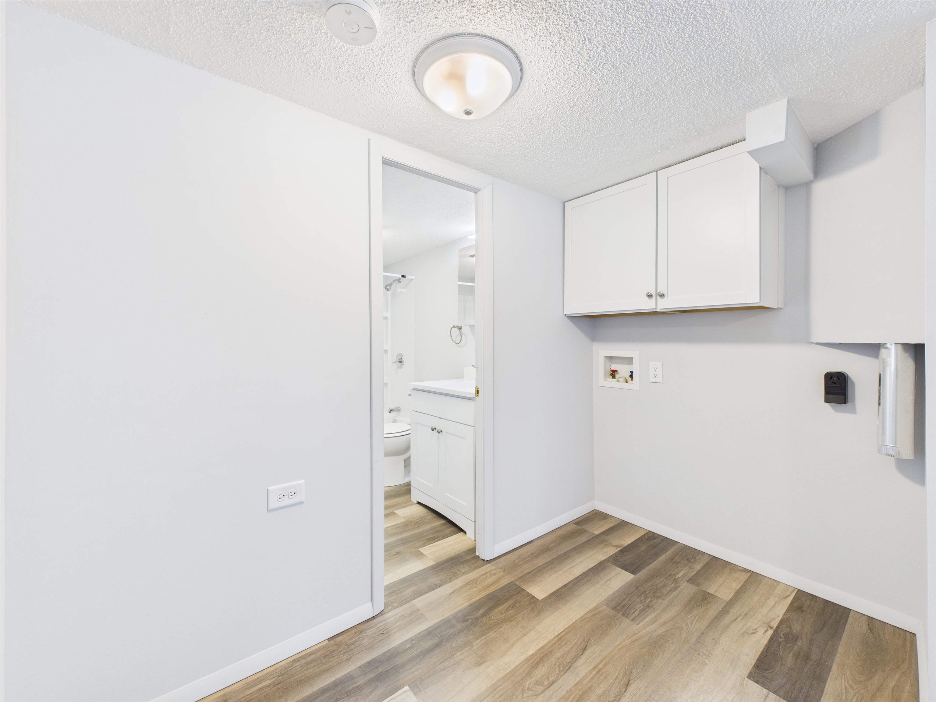 Laundry room featuring a textured ceiling, washer hookup, light wood-style floors, and cabinet space