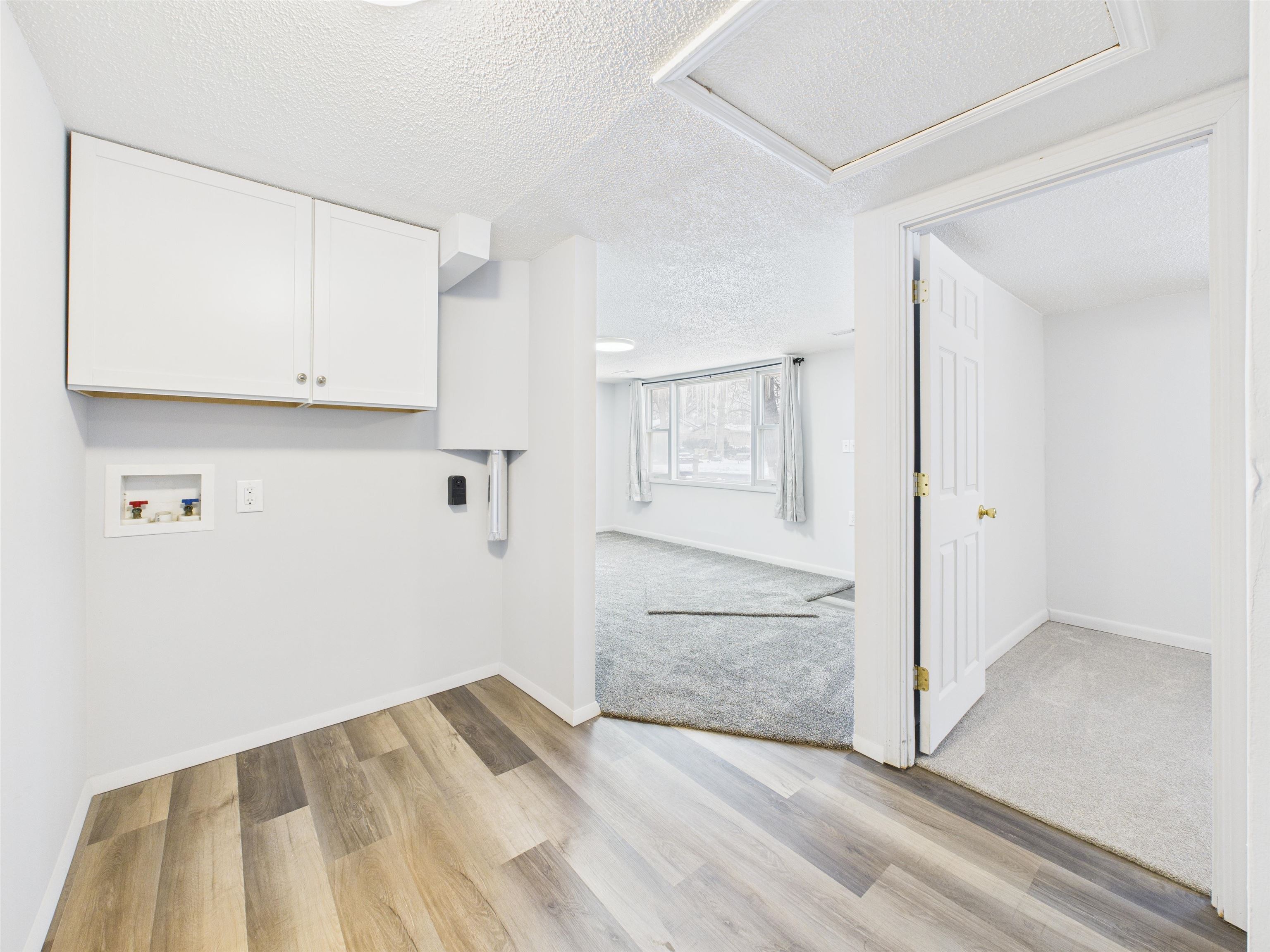 Laundry area with a textured ceiling, hookup for a washing machine, light wood-type flooring, and cabinet space