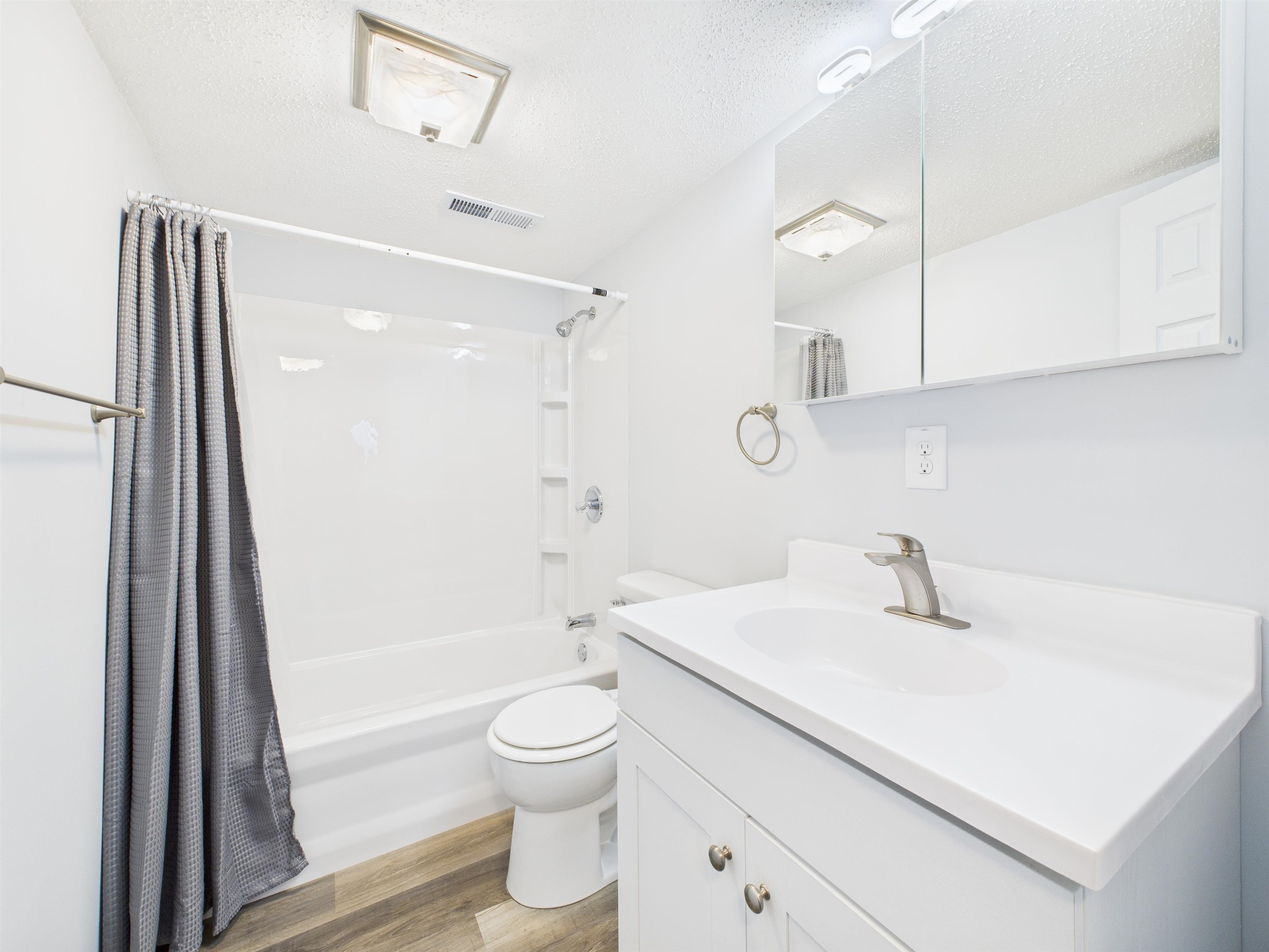 Bathroom with shower / bath combination with curtain, a textured ceiling, light wood-style flooring, and vanity