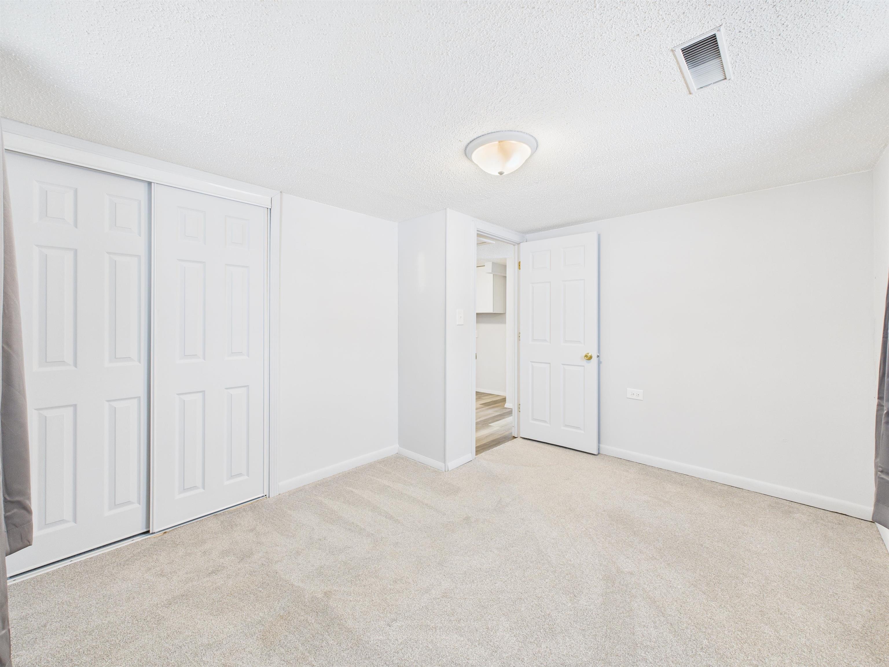 Unfurnished bedroom with a textured ceiling, light carpet, and a closet