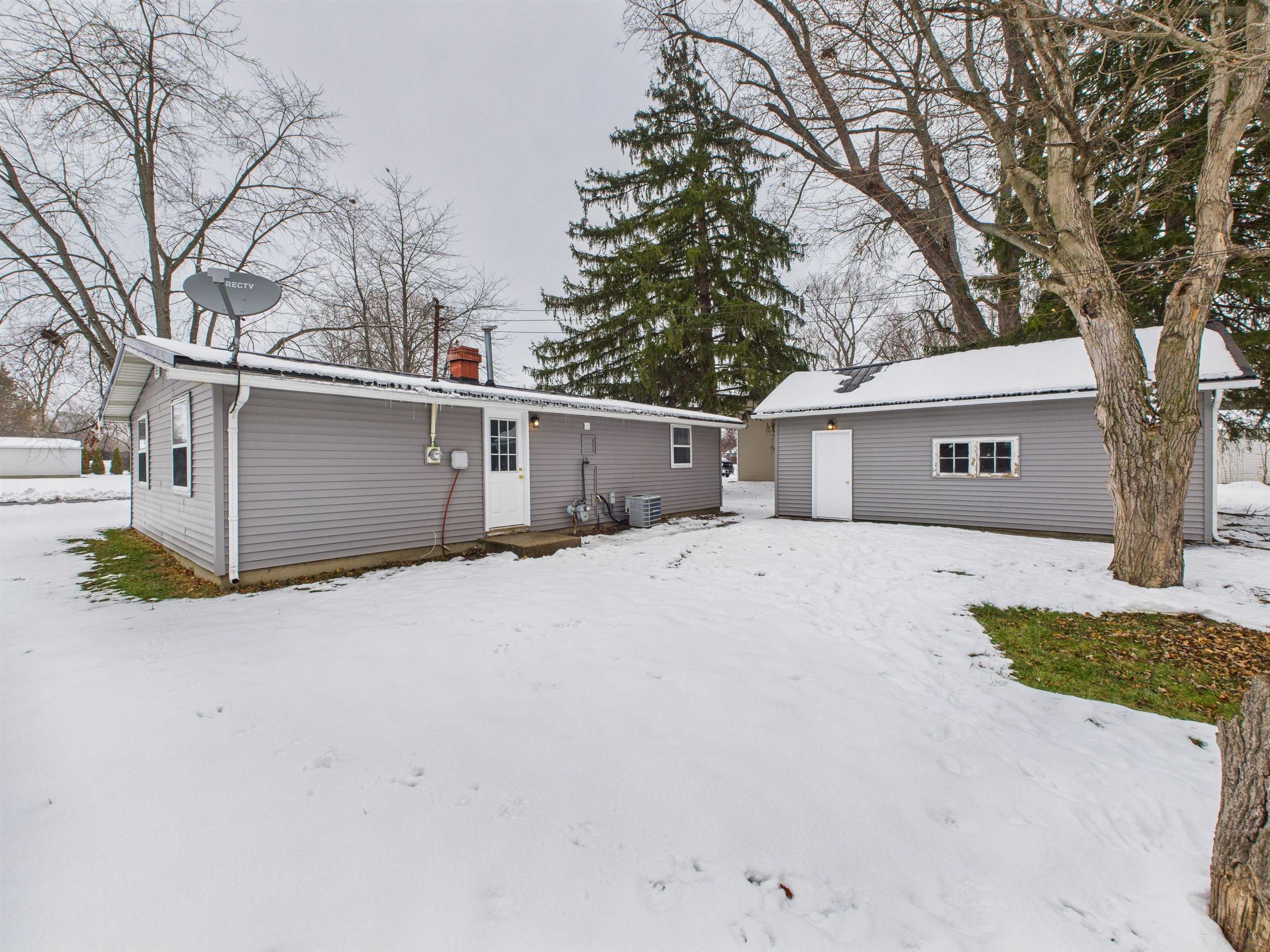 Snow covered house featuring a chimney and an outdoor structure
