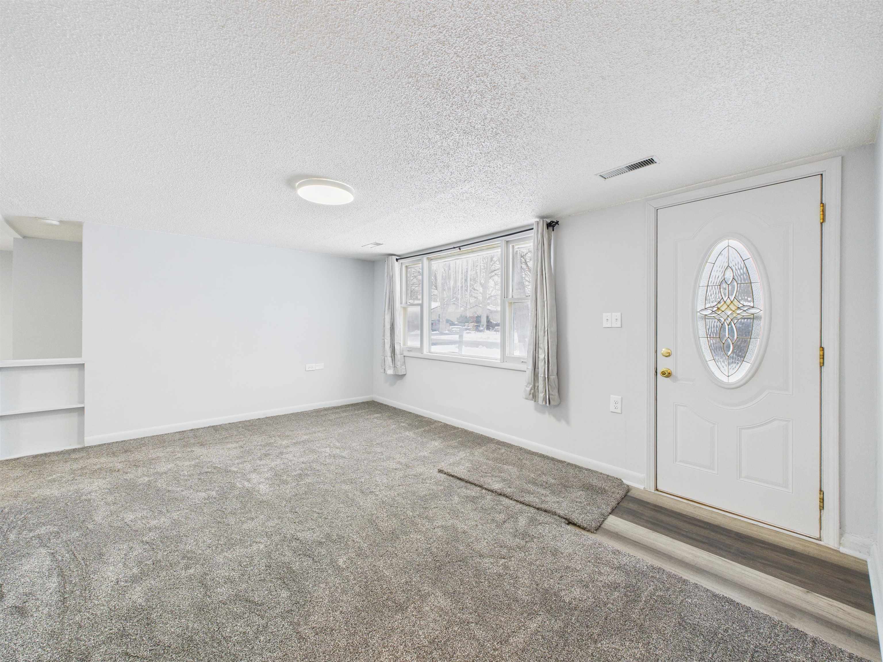 Carpeted foyer entrance with a textured ceiling and healthy amount of natural light