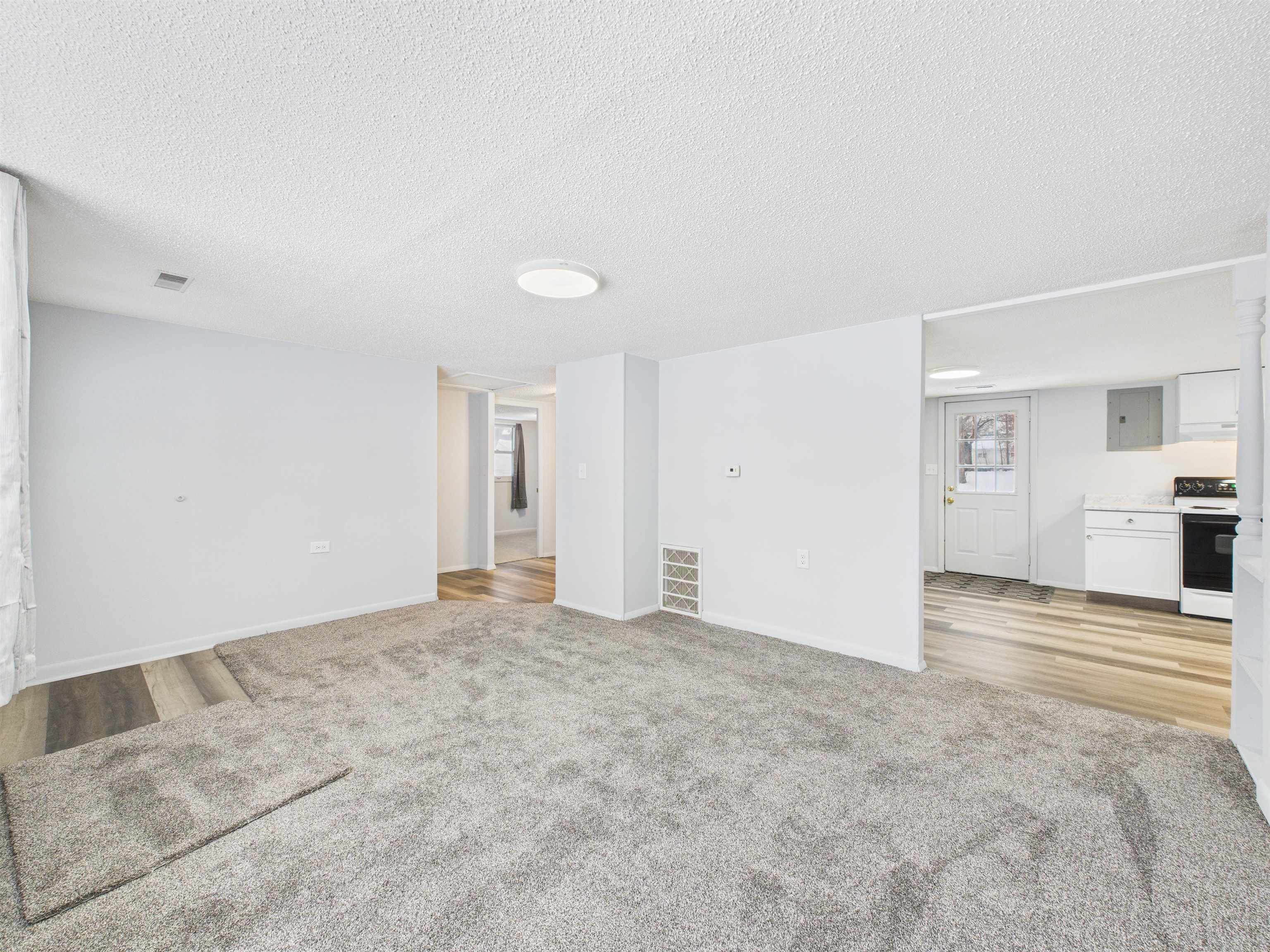 Unfurnished living room featuring a textured ceiling, light carpet, and light wood-type flooring