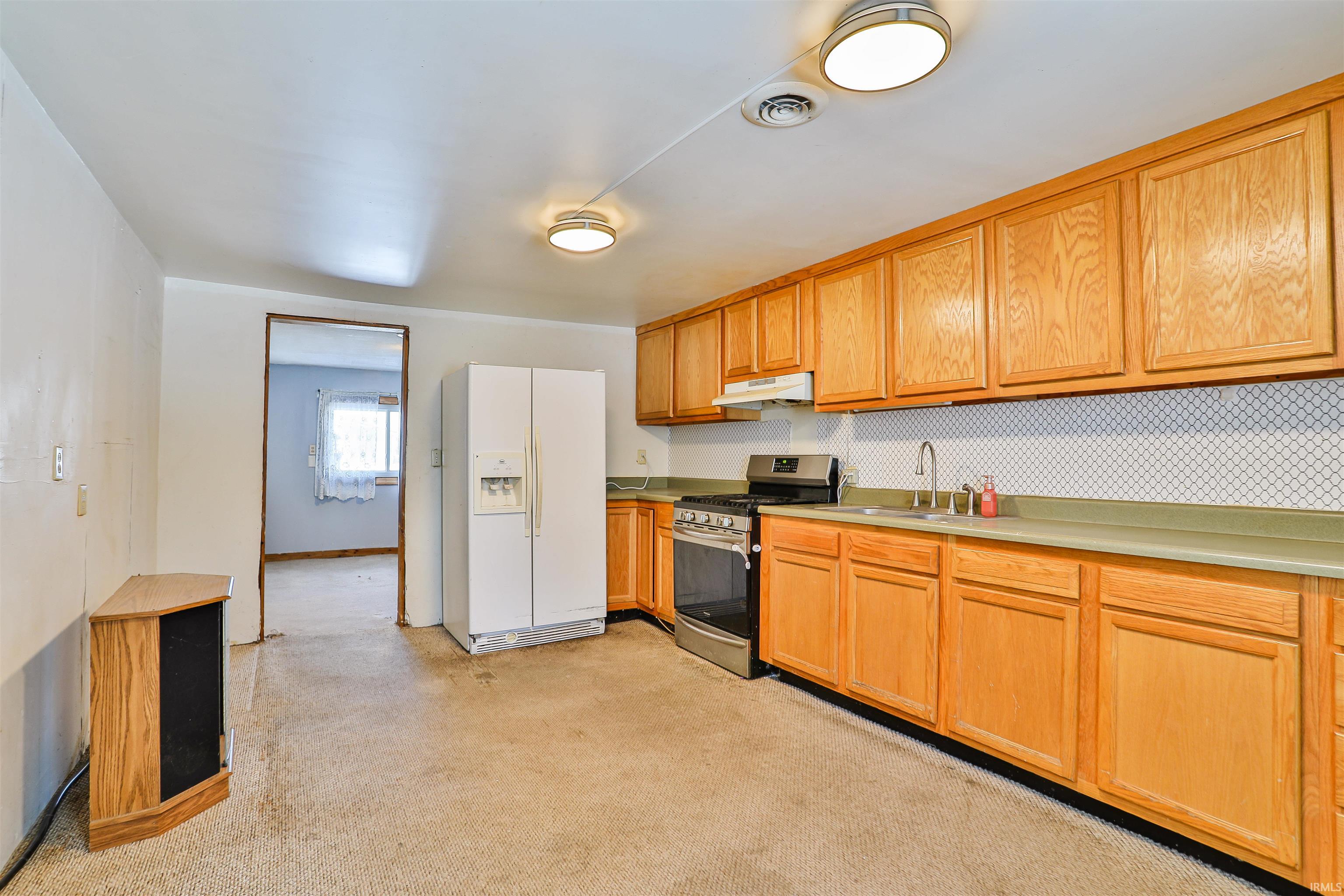 Kitchen with stainless steel range with gas cooktop, white refrigerator with ice dispenser, light countertops, and under cabinet range hood