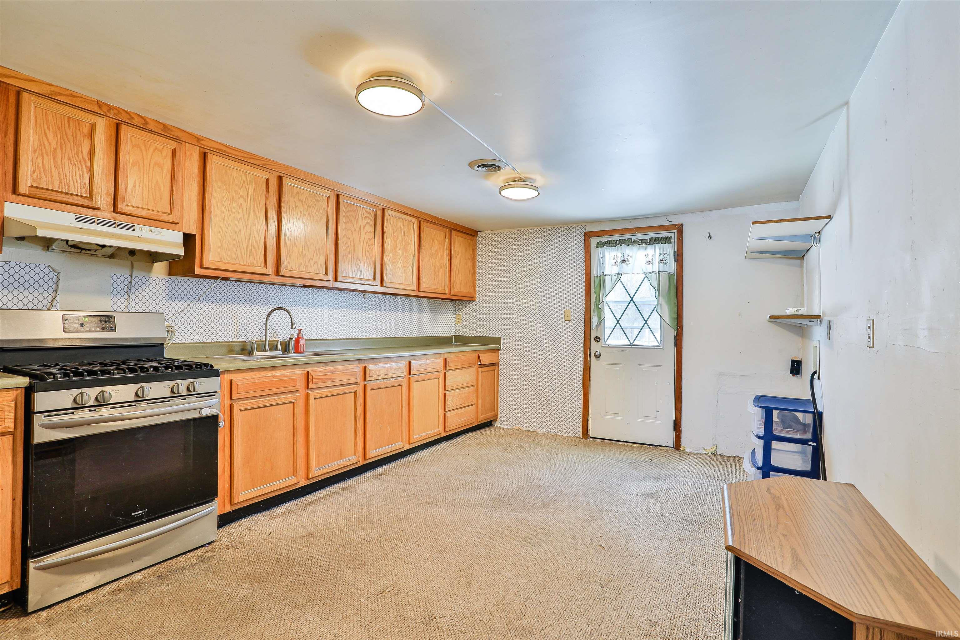 Kitchen featuring stainless steel gas range oven, under cabinet range hood, light countertops, and light carpet