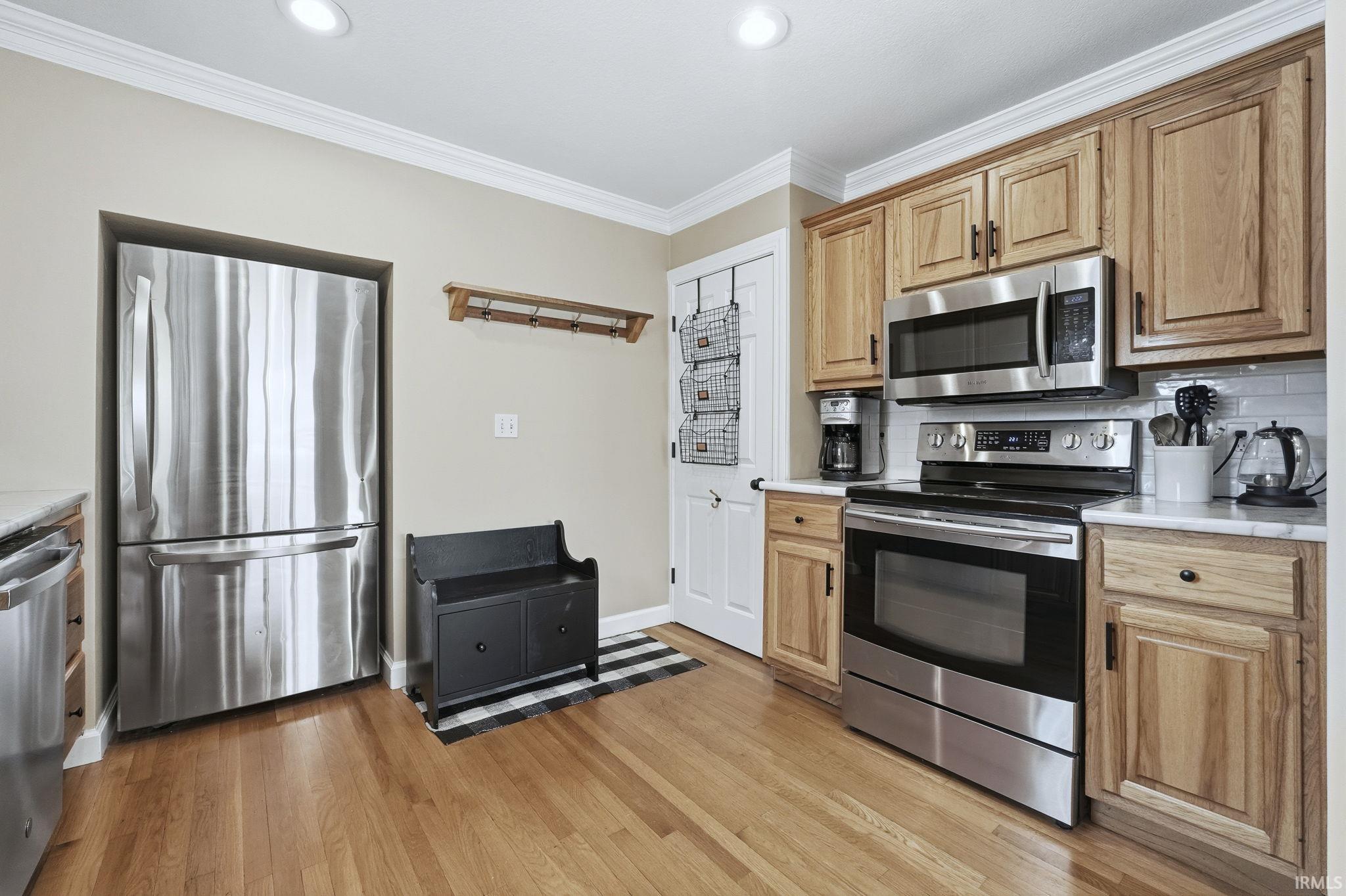 Kitchen with stainless steel appliances, light countertops, tasteful backsplash, ornamental molding, and light wood finished floors