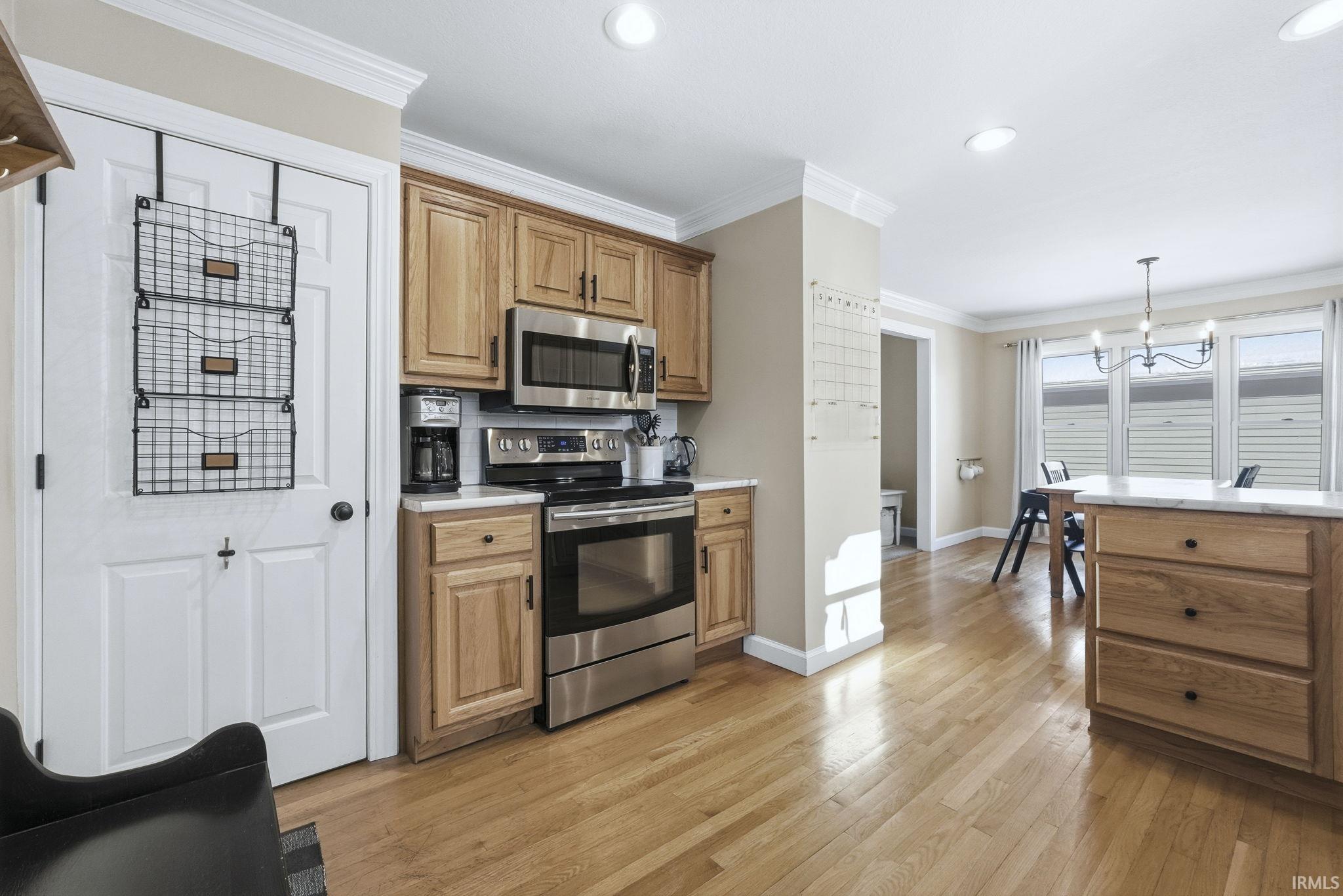 Kitchen featuring stainless steel appliances, ornamental molding, light countertops, light wood finished floors, and hanging light fixtures