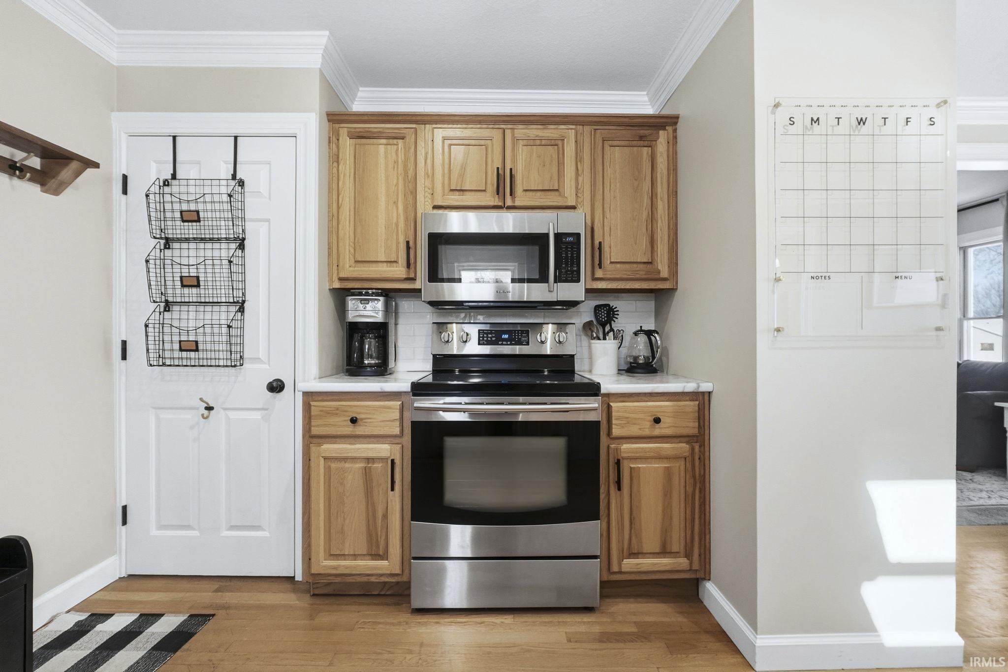 Kitchen with appliances with stainless steel finishes, light countertops, light wood-type flooring, backsplash, and crown molding
