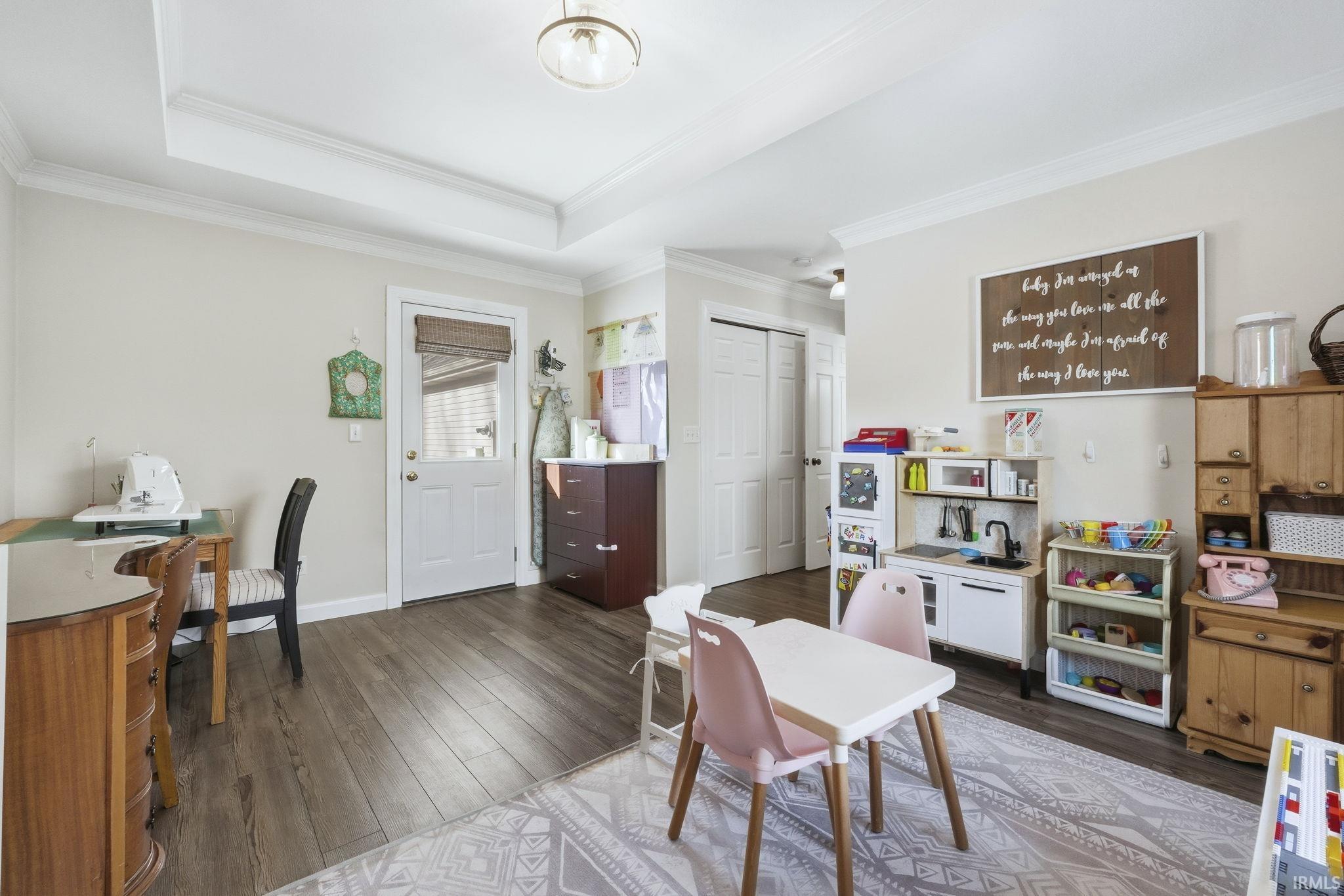 Home office with dark wood-style flooring, ornamental molding, and a tray ceiling