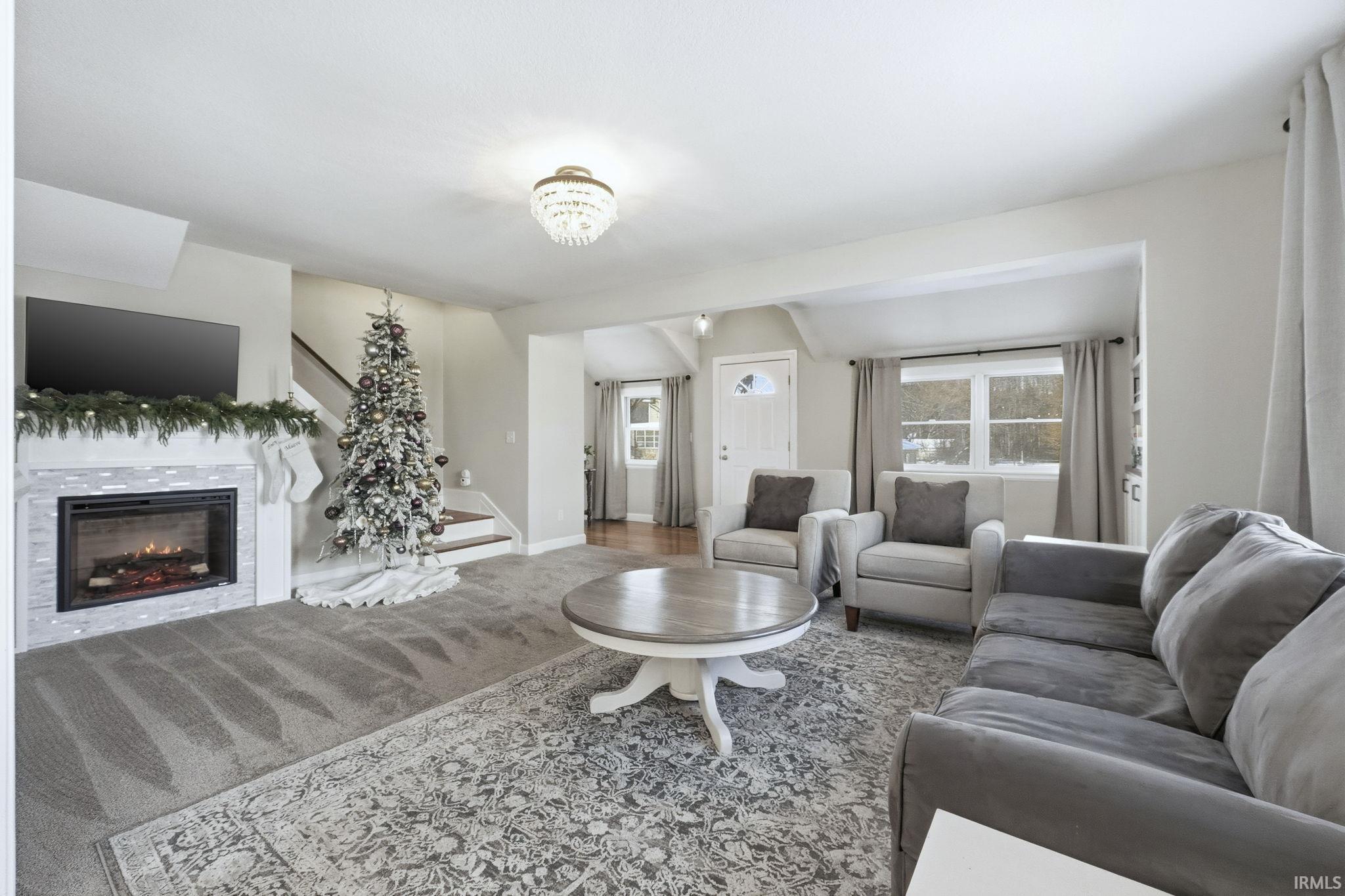Living room featuring a tiled fireplace, carpet, stairway, a chandelier, and vaulted ceiling