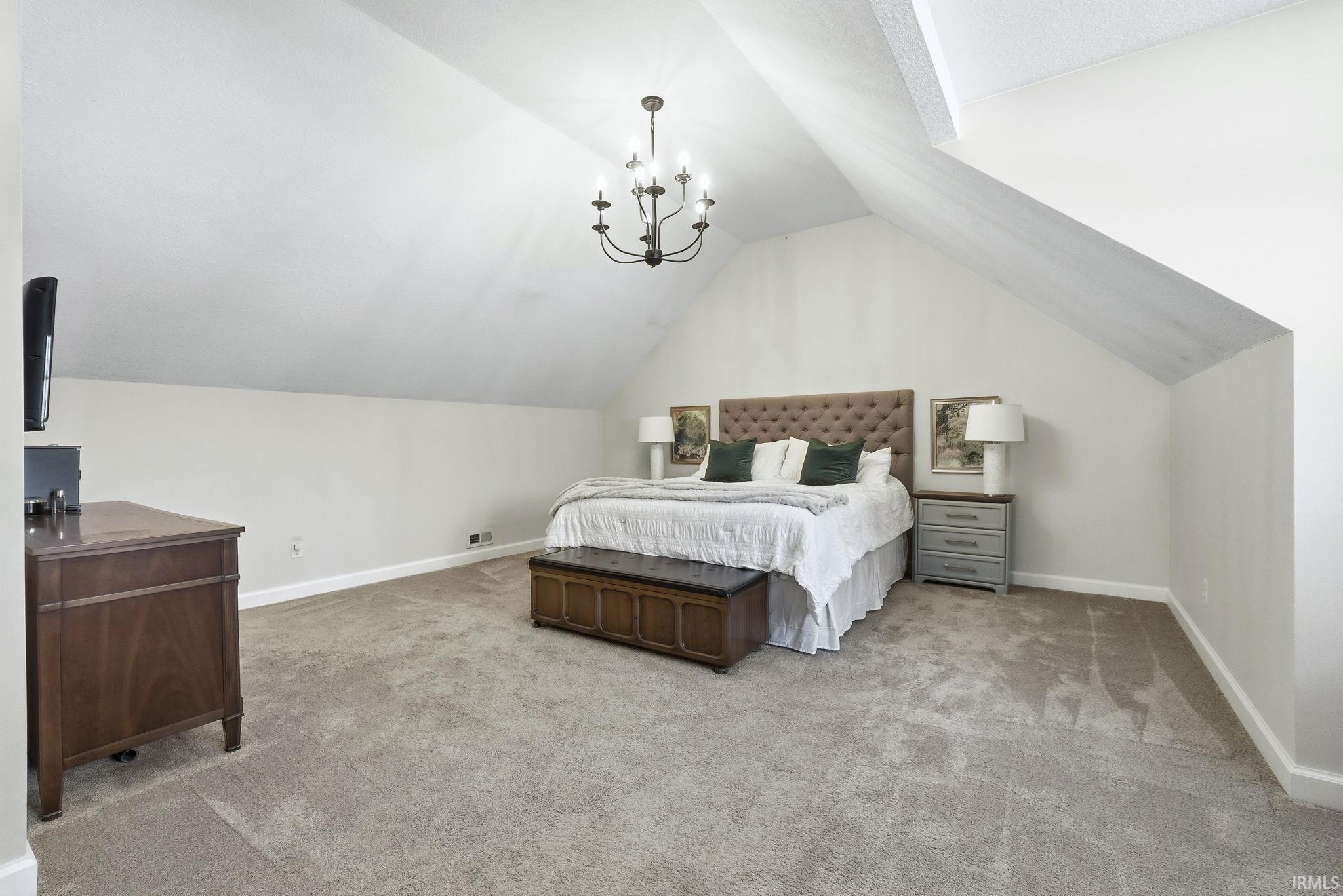 Bedroom with light carpet, a chandelier, and vaulted ceiling