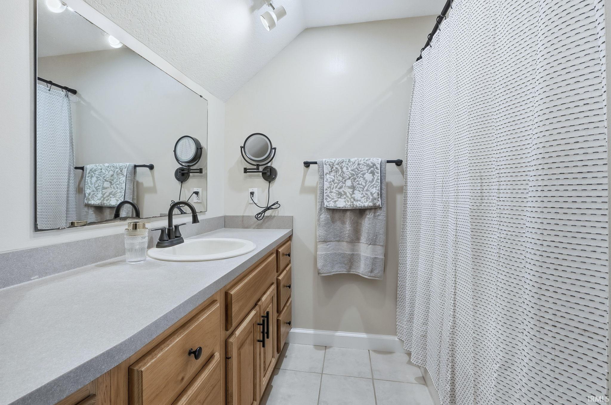 Bathroom with vanity, a shower with curtain, light tile patterned floors, and vaulted ceiling
