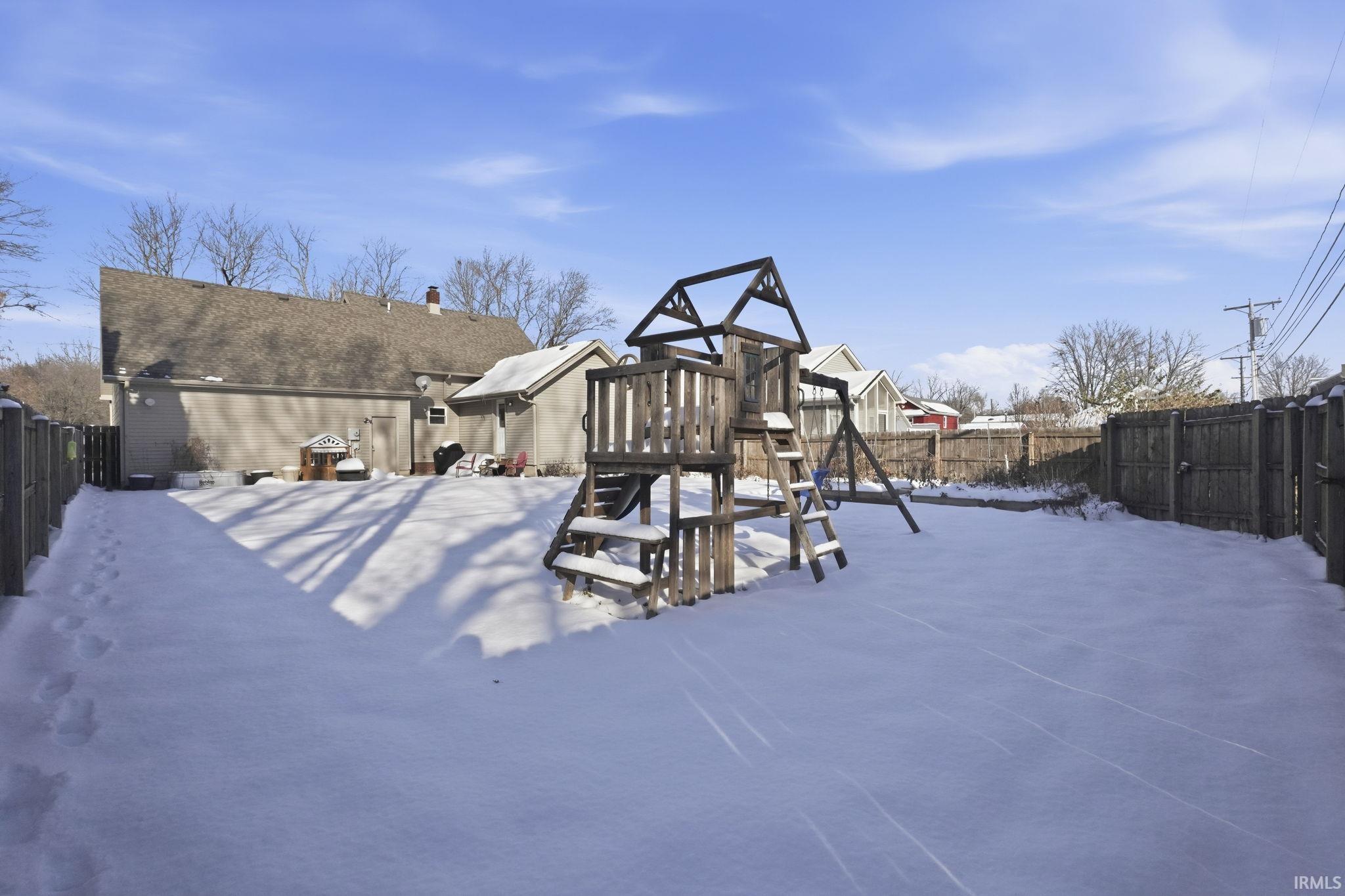 Snowy yard with a fenced backyard, a playground, and a patio