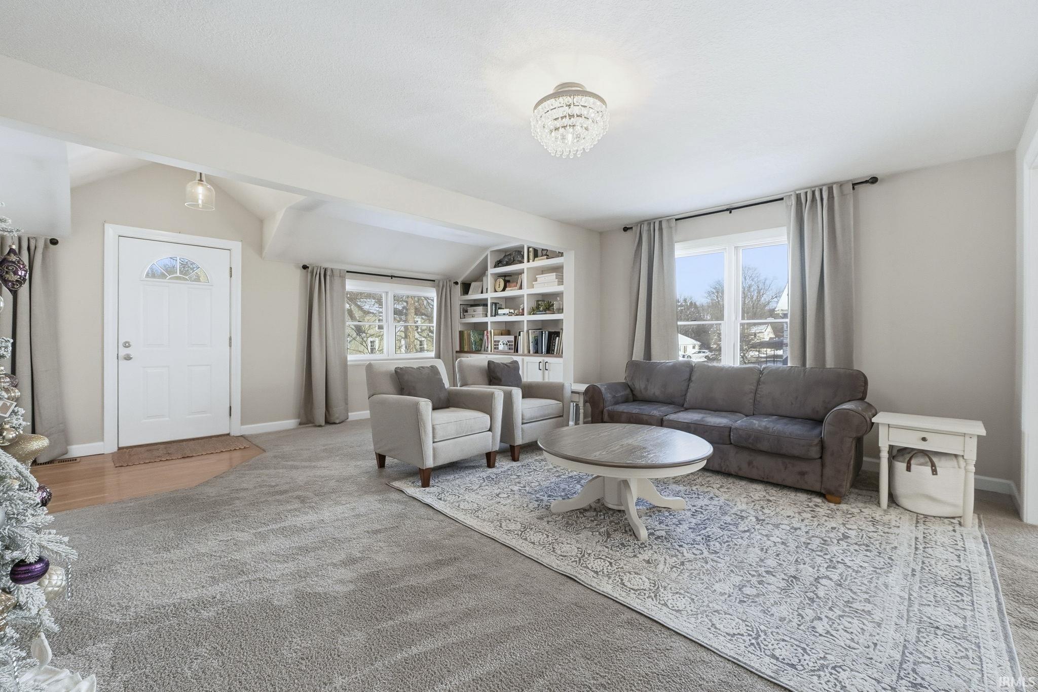 Carpeted living area featuring vaulted ceiling and a chandelier