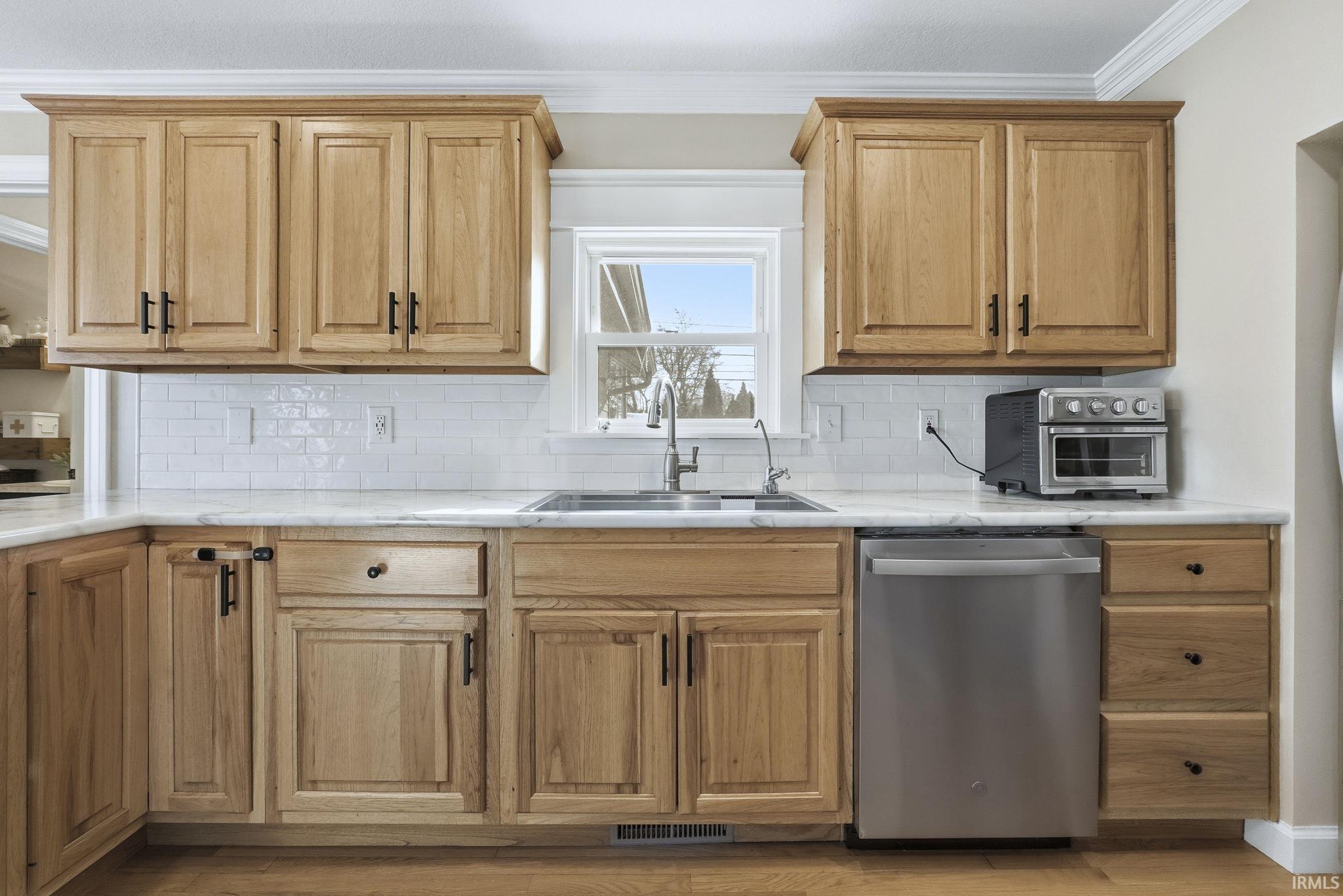 Kitchen featuring stainless steel dishwasher, ornamental molding, backsplash, and light wood-type flooring