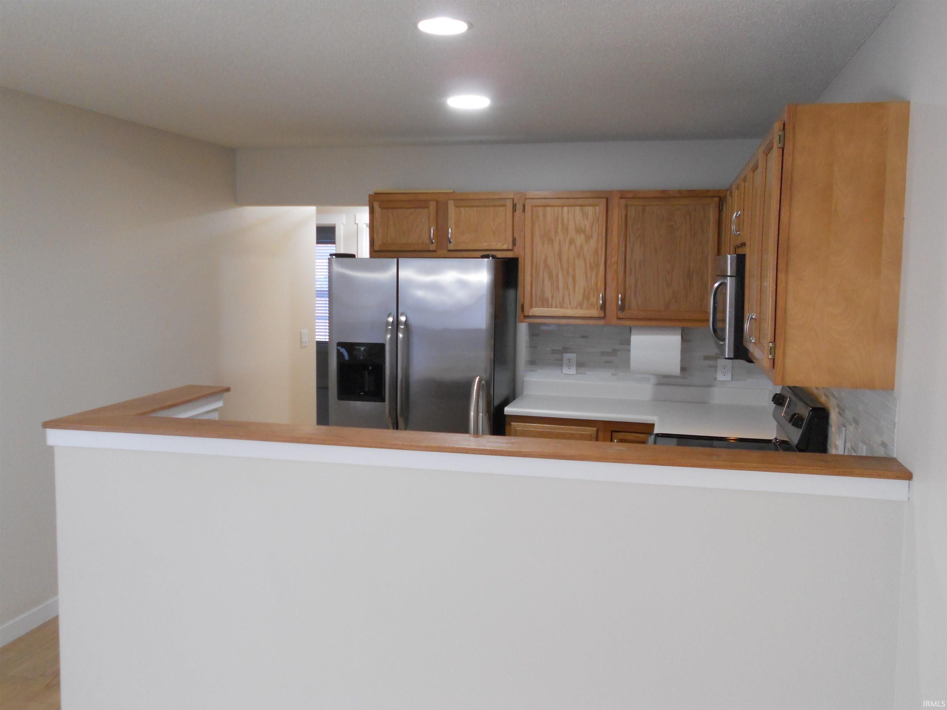 Kitchen featuring appliances with stainless steel finishes, light countertops, a peninsula, backsplash, and recessed lighting