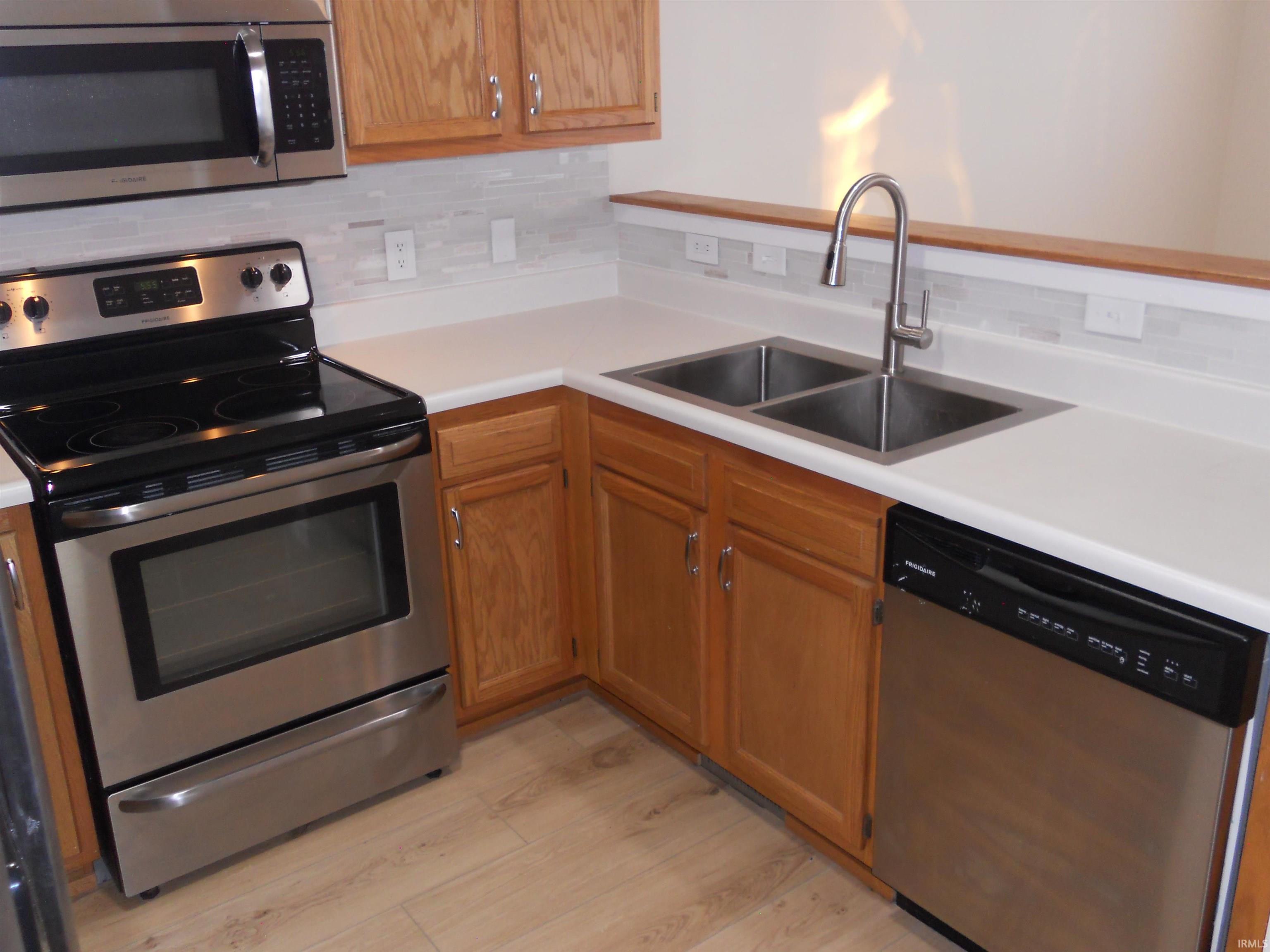 Kitchen with stainless steel appliances, light countertops, decorative backsplash, and light wood-type flooring