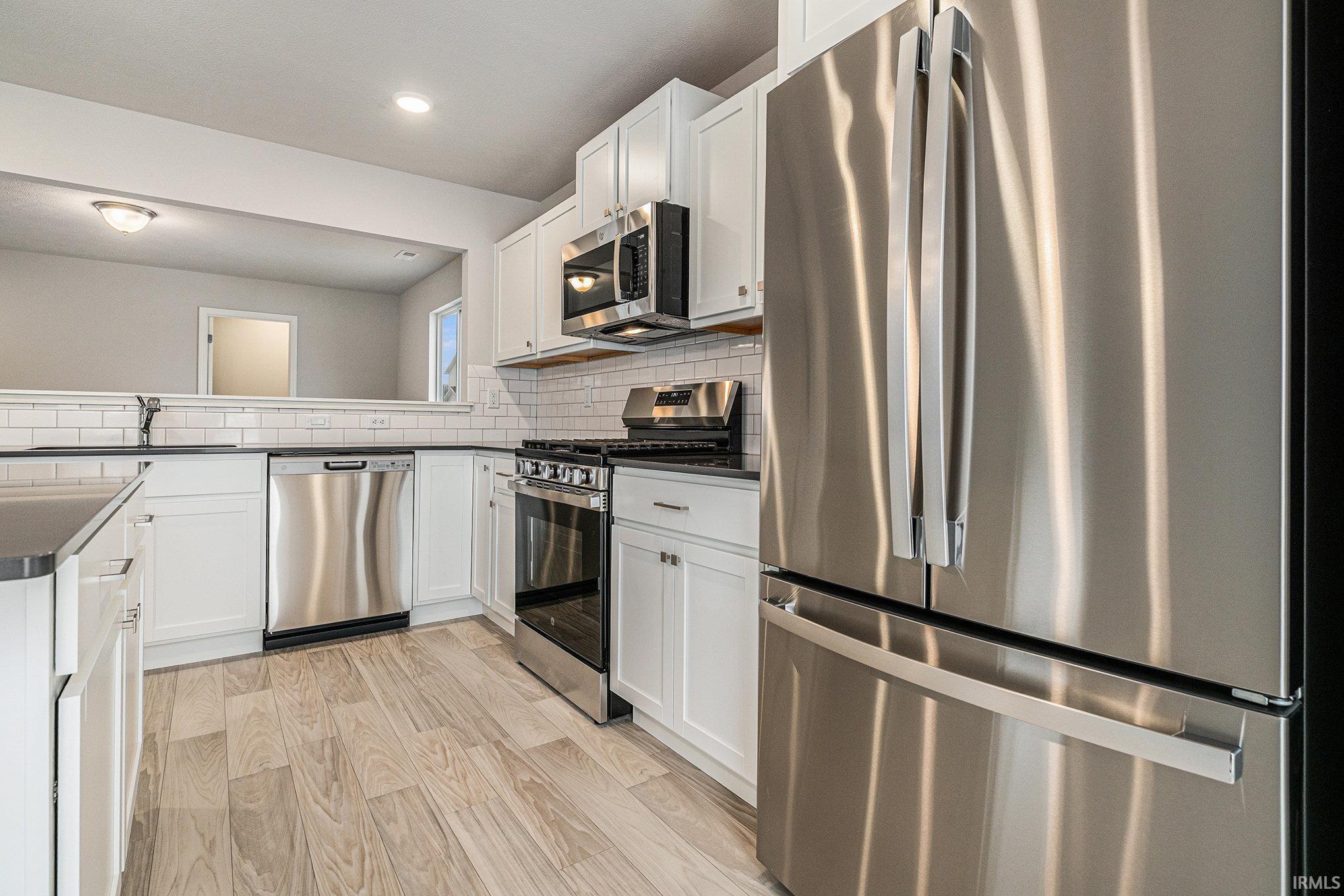 The kitchen includes a center island for additional storage and prep space.  The extended edge can fit barstools and there is pendant lighting above. Quartz counters are accented by subway tile backsplash and select stainless steel appliances included