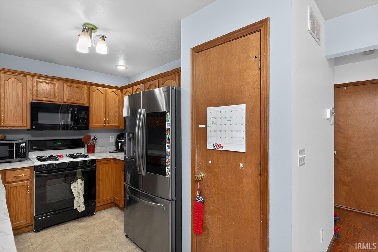 Kitchen featuring gas stove, stainless steel fridge with ice dispenser, brown cabinetry, and black microwave