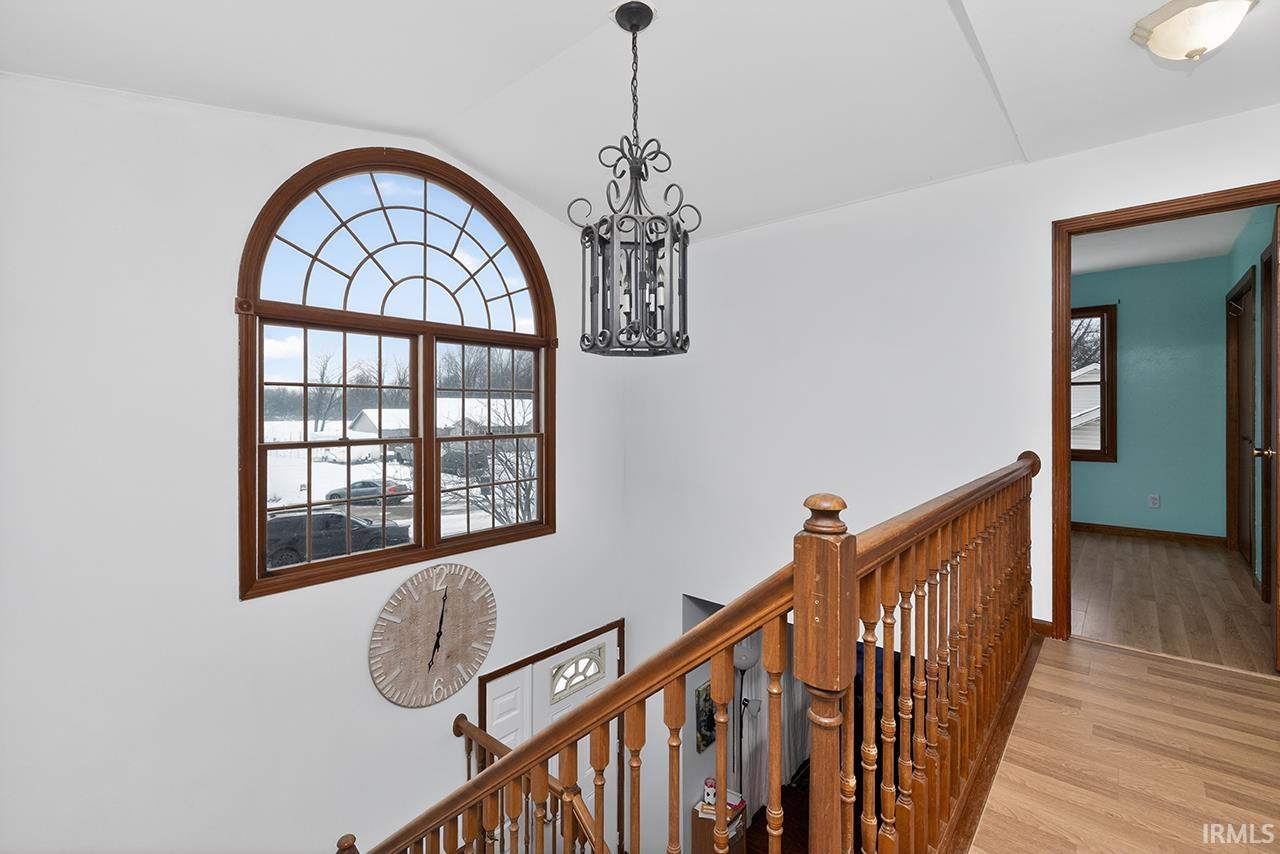 Hallway with a chandelier, an upstairs landing, wood finished floors, and lofted ceiling