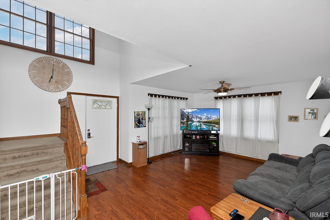 Living room with dark wood finished floors, stairway, a ceiling fan, and a high ceiling