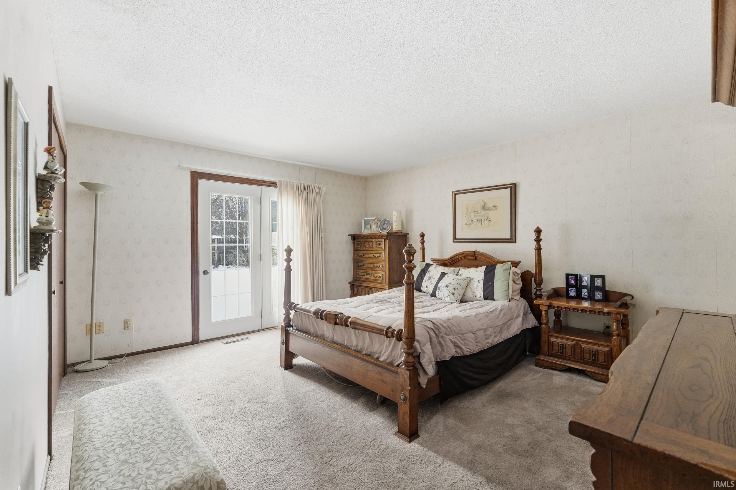 Bedroom featuring carpet flooring, access to outside, a textured ceiling, and wallpapered walls