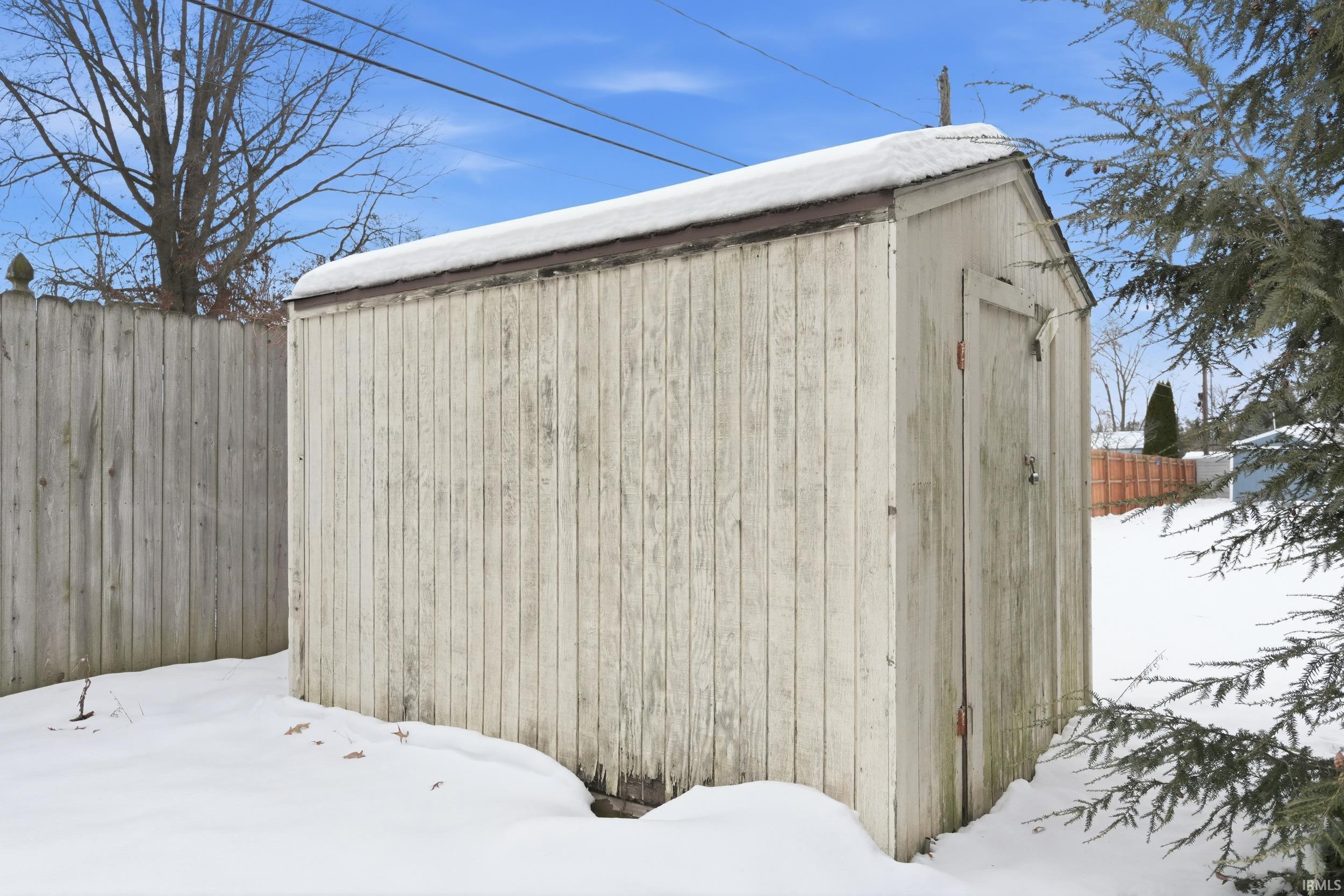 Snow covered structure featuring a storage unit and a fenced backyard