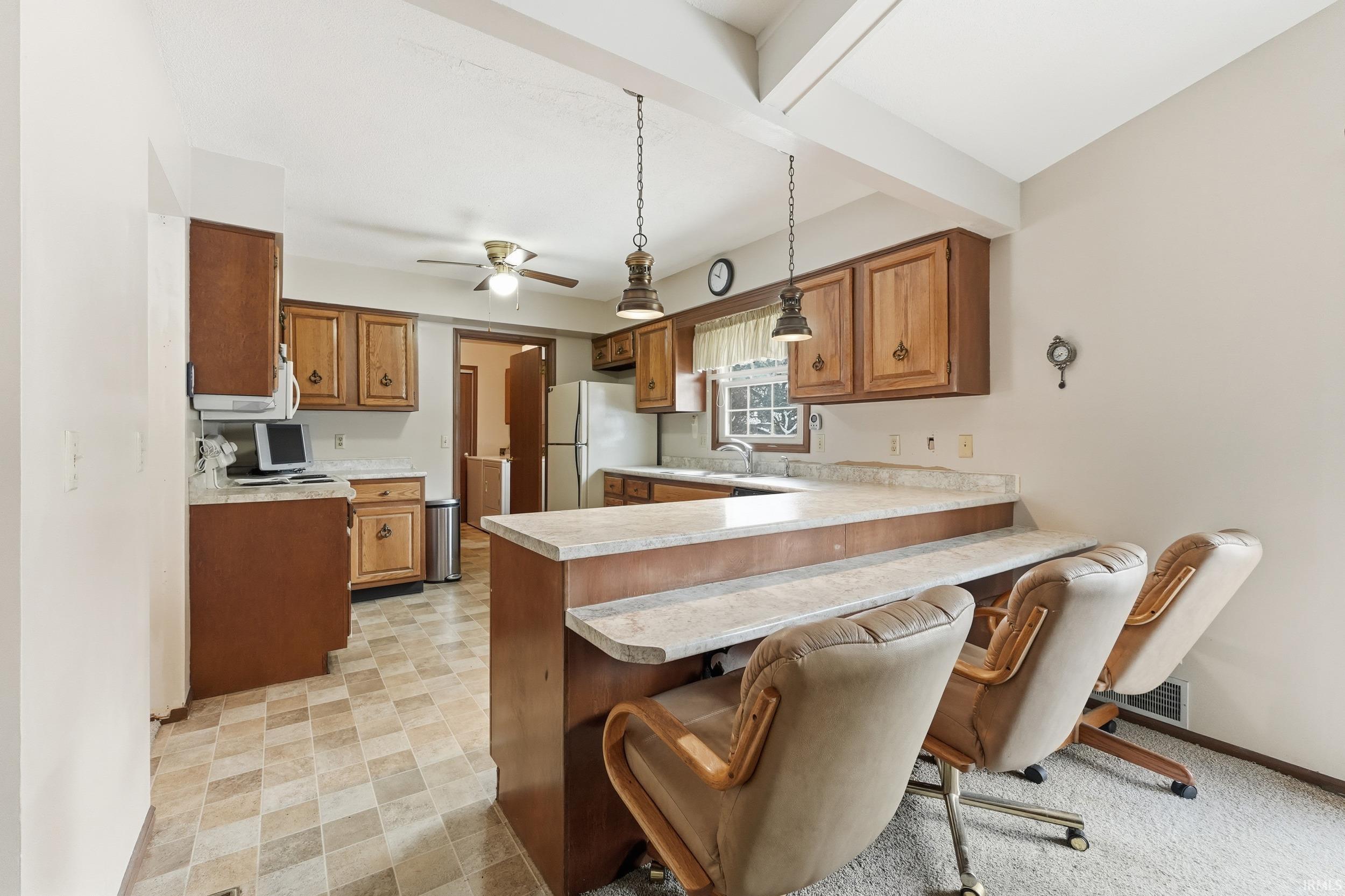Kitchen featuring light countertops, a kitchen breakfast bar, a peninsula, brown cabinetry, and white appliances