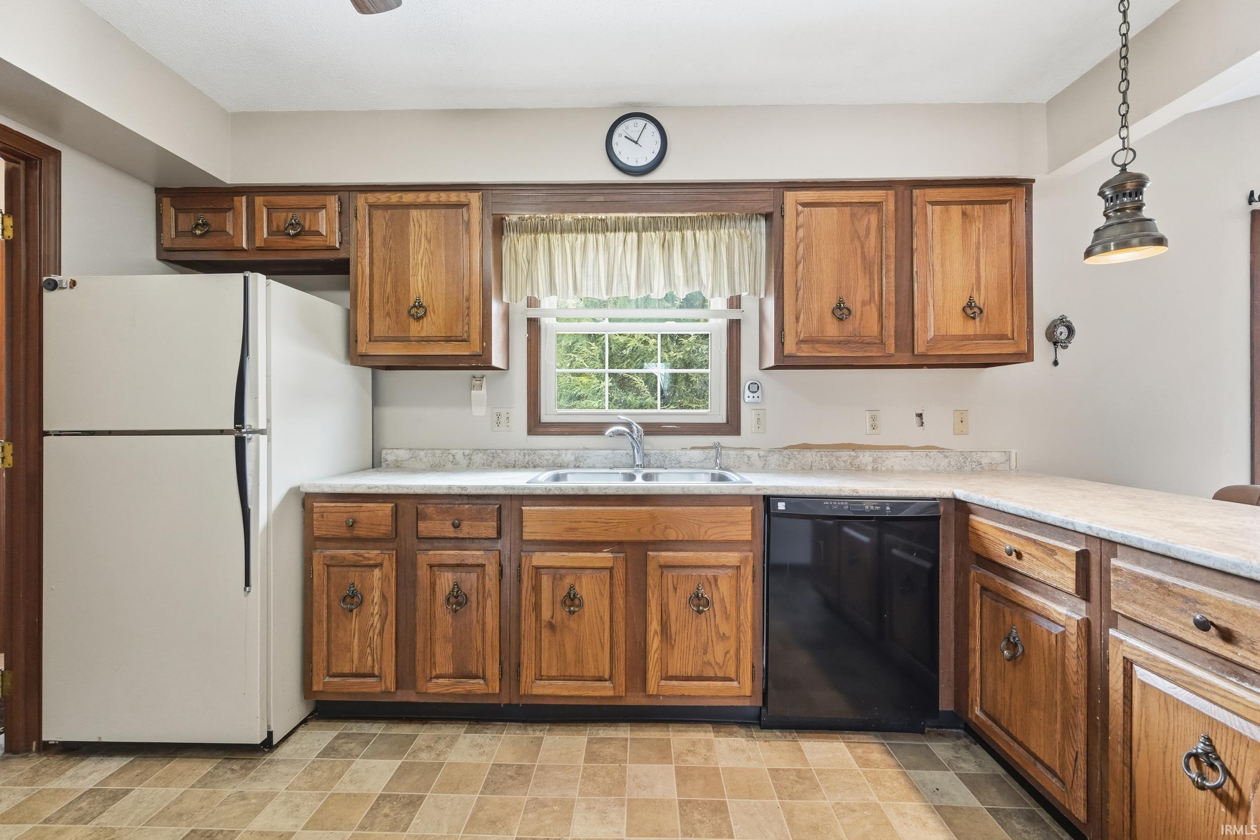 Kitchen with freestanding refrigerator, dishwasher, brown cabinets, light countertops, and hanging light fixtures