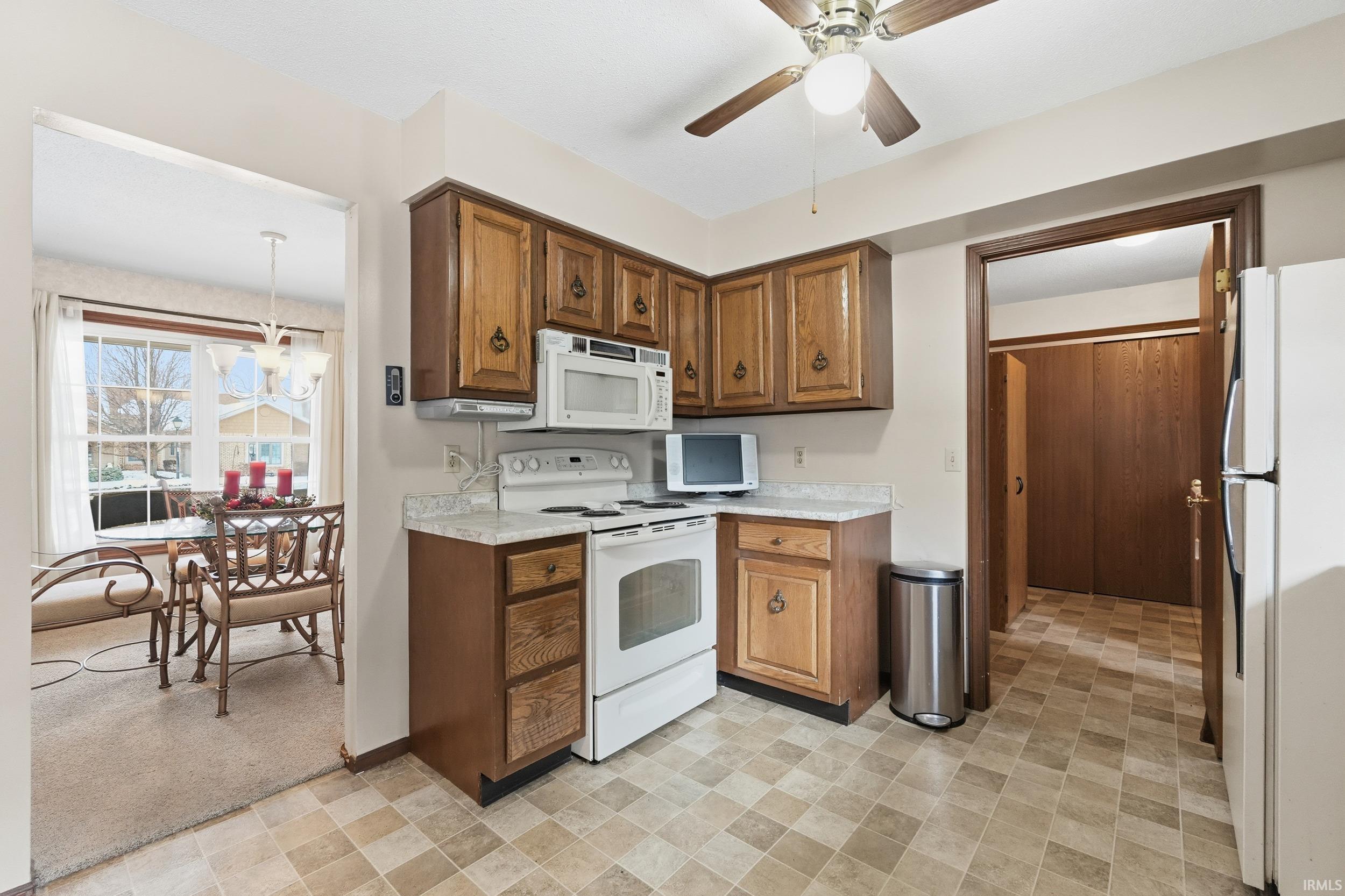 Kitchen with white appliances, light countertops, brown cabinetry, ceiling fan, and light flooring