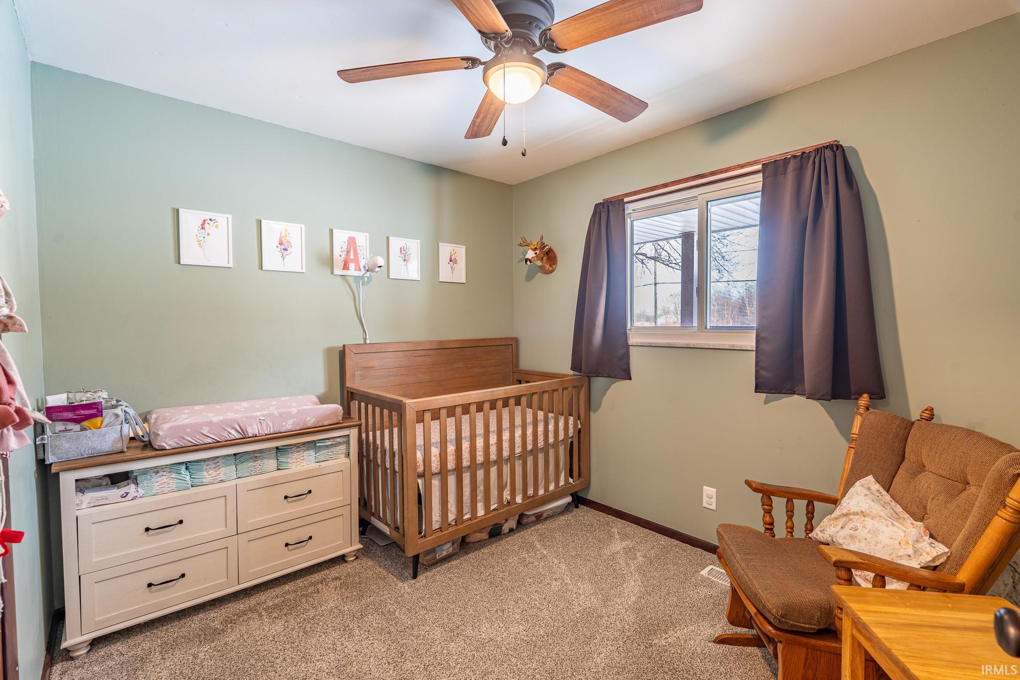 Bedroom with light colored carpet, ceiling fan, and a crib