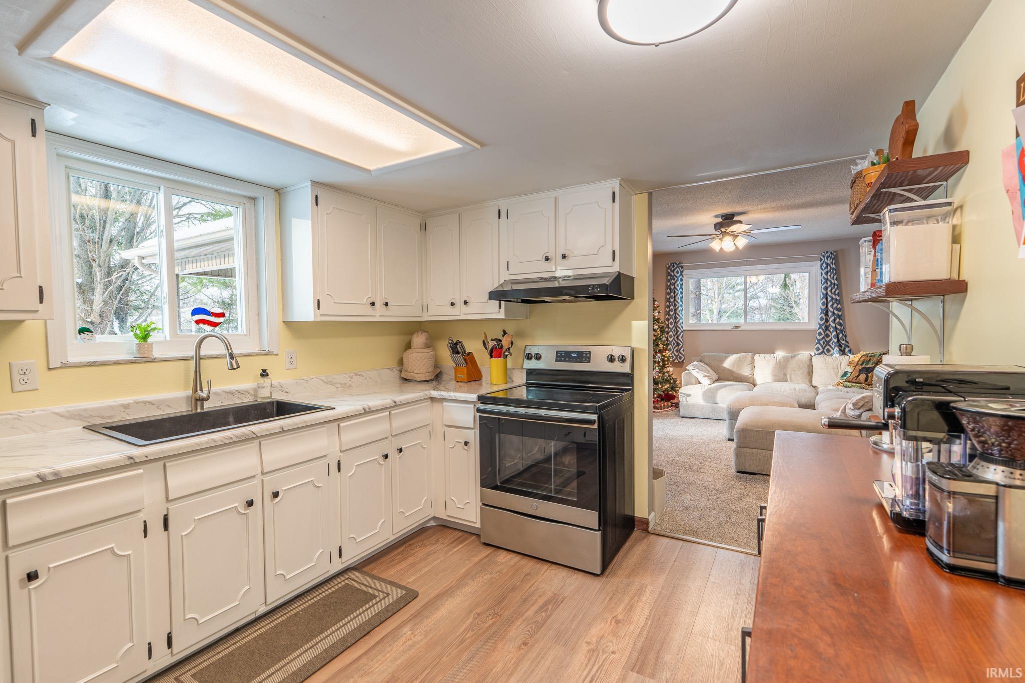 Kitchen featuring stainless steel range with electric cooktop, light wood-style floors, white cabinets, under cabinet range hood, and light countertops