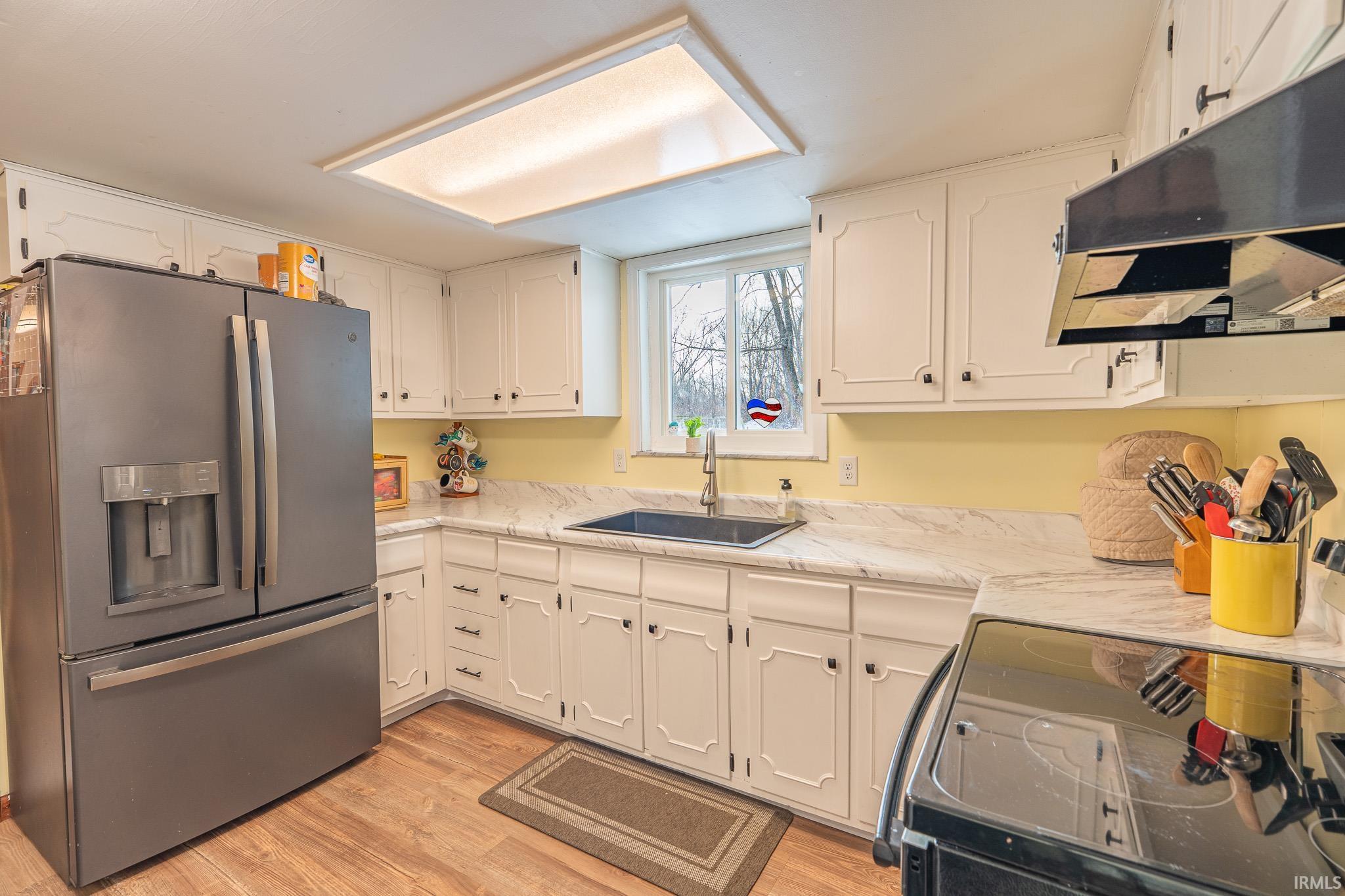 Kitchen featuring stainless steel refrigerator with ice dispenser, range with electric stovetop, under cabinet range hood, light wood-style flooring, and white cabinets